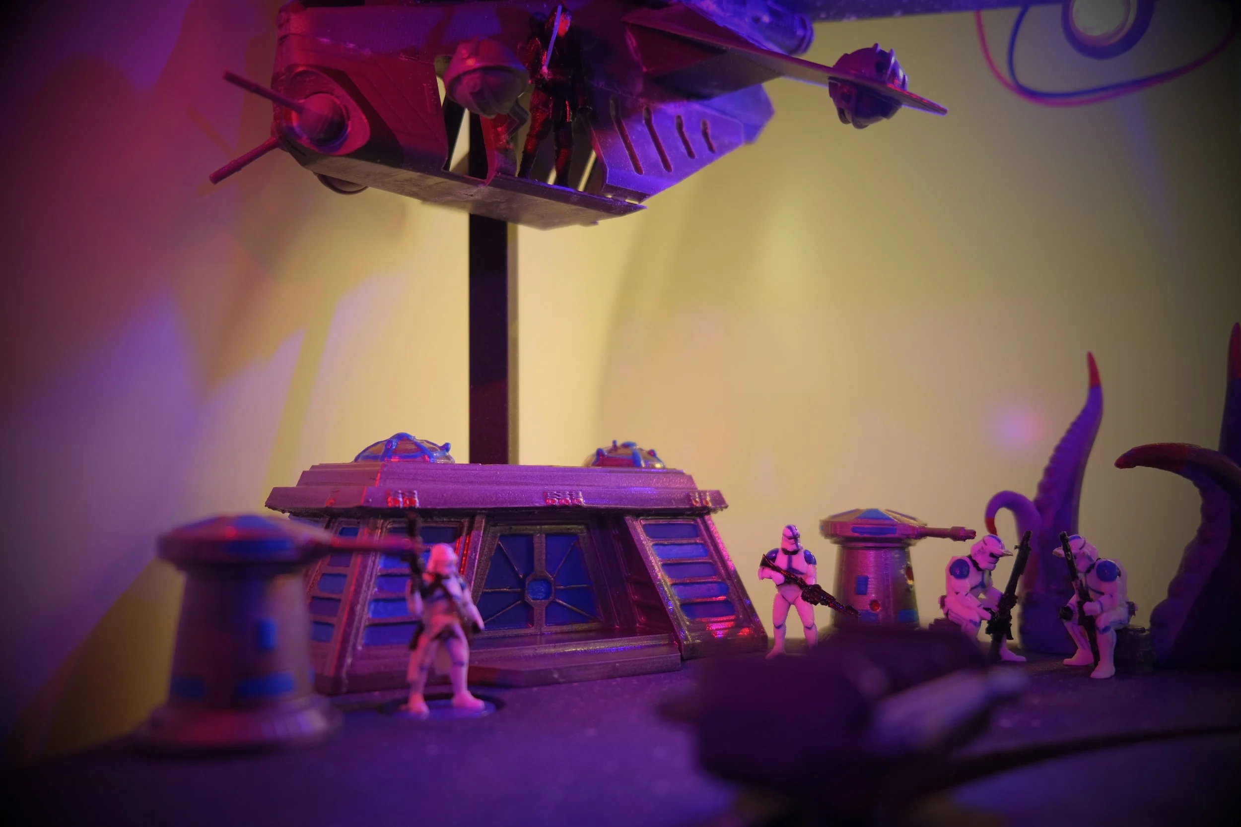 A display of Star Wars toy figures, including AT-ATs and soldiers, under purple and yellow lighting.