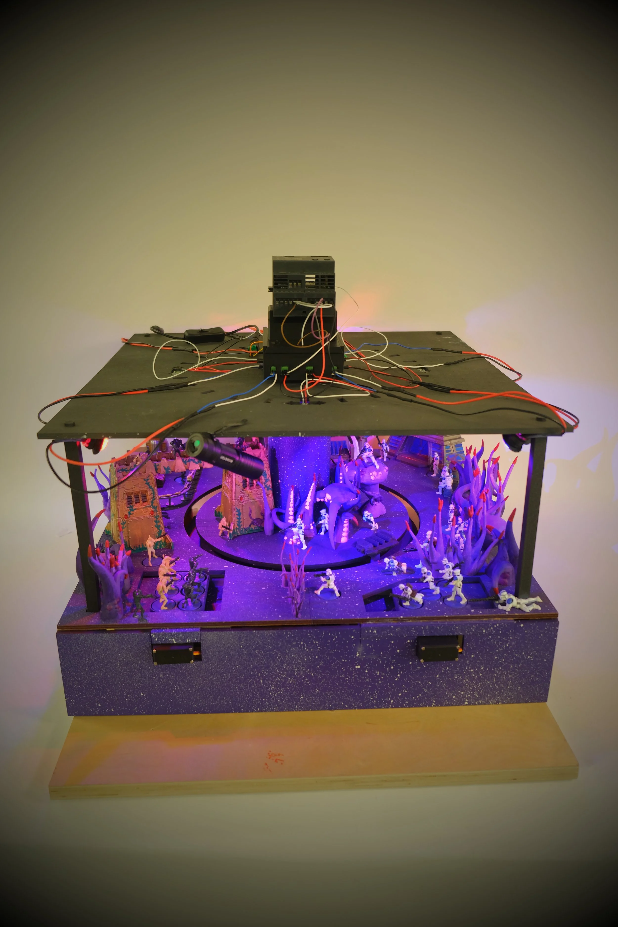 A tabletop display featuring a miniature fantasy scene with toy soldiers, a small tower, and illuminated trees, set on a speckled black base.