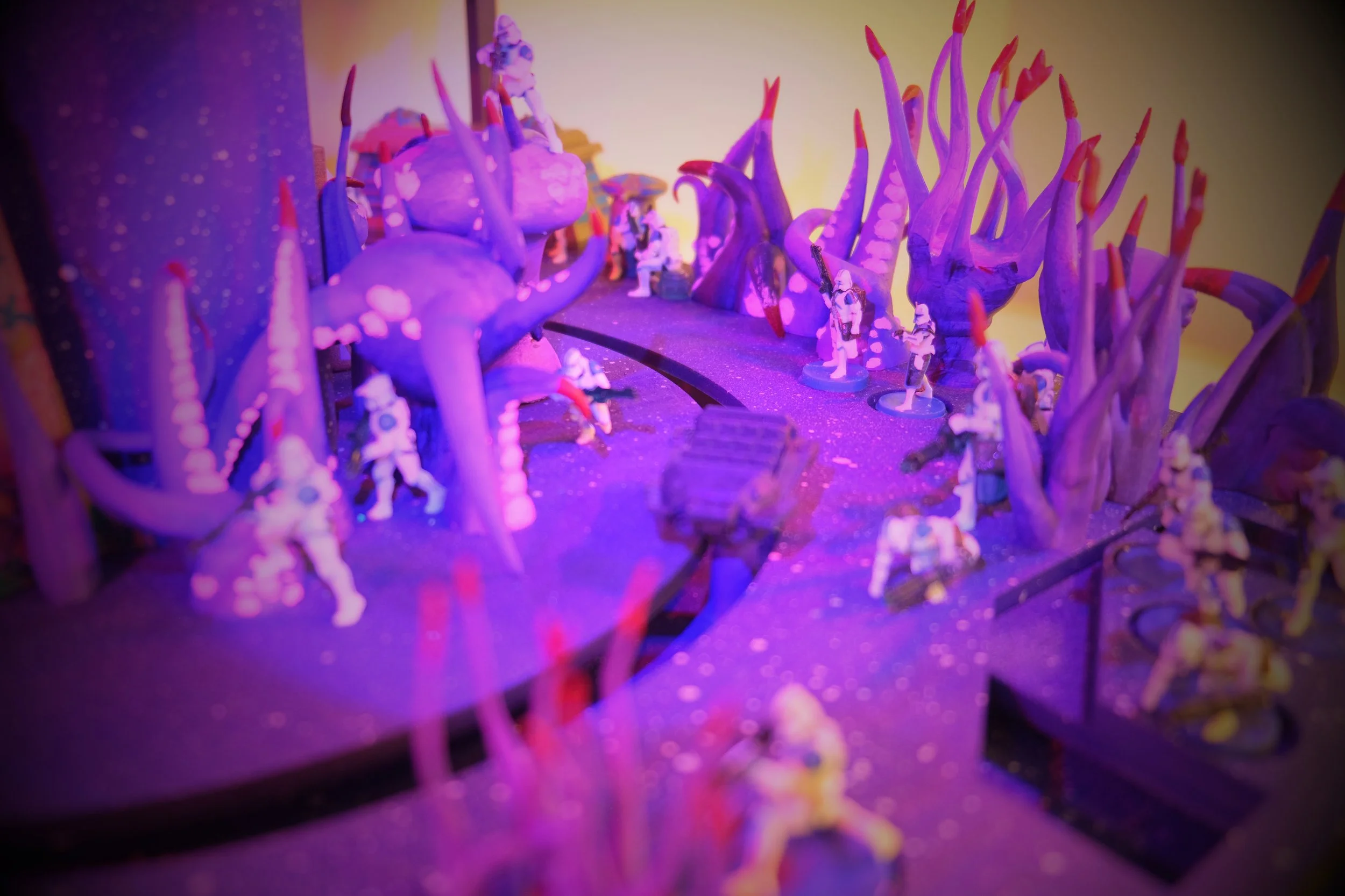 Miniature soldiers and fantasy trees illuminated by purple and pink lighting in a diorama scene.