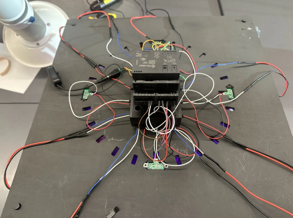 Multiple wires connected to a relay on a gray surface, with small circuit boards and a lamp in the background, suggesting an electronics or robotics project.