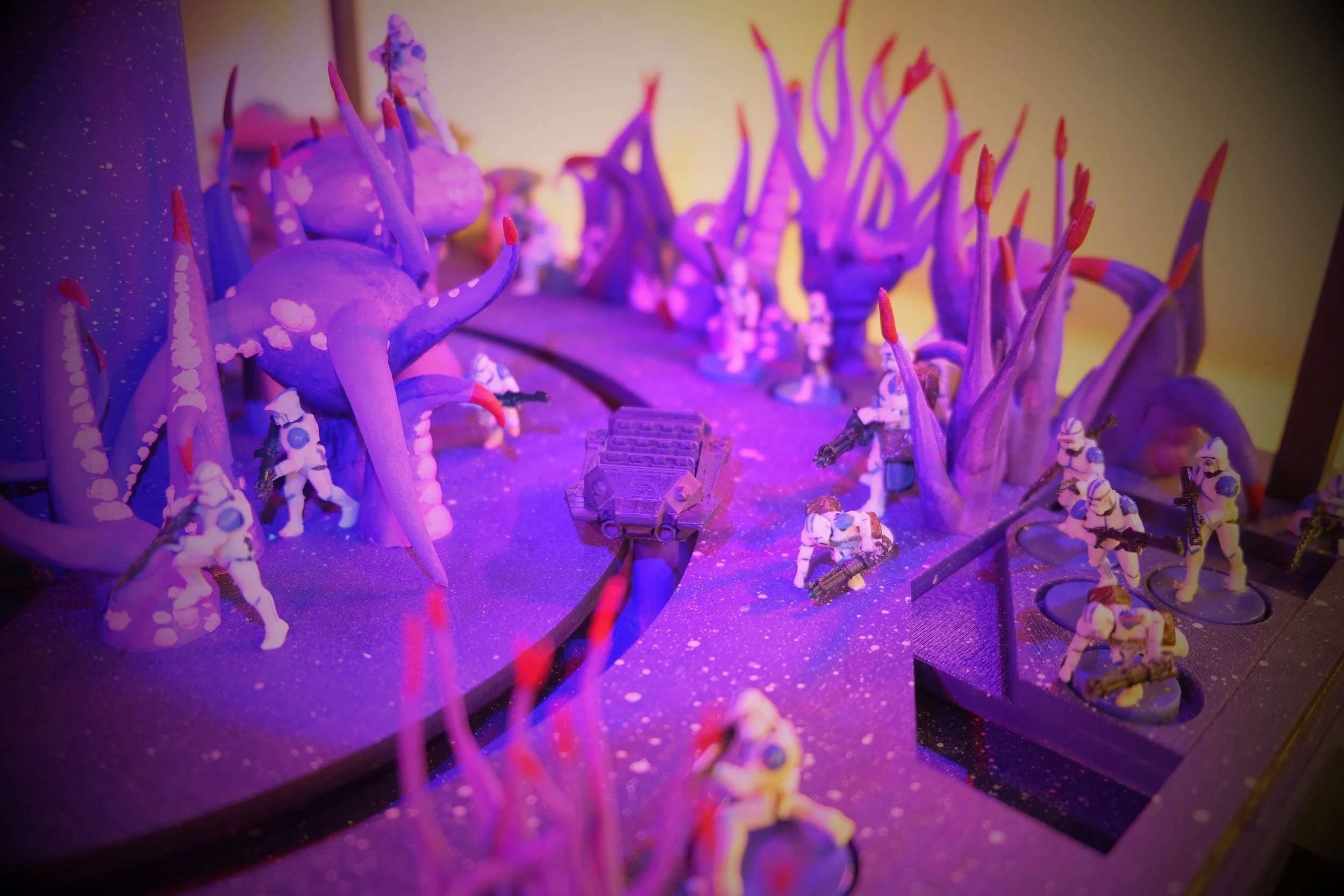Miniature Star Wars figures, including Stormtroopers, are set among purple alien-like tentacles and plants, with a sci-fi themed terrain, illuminated by purple and pink lighting.