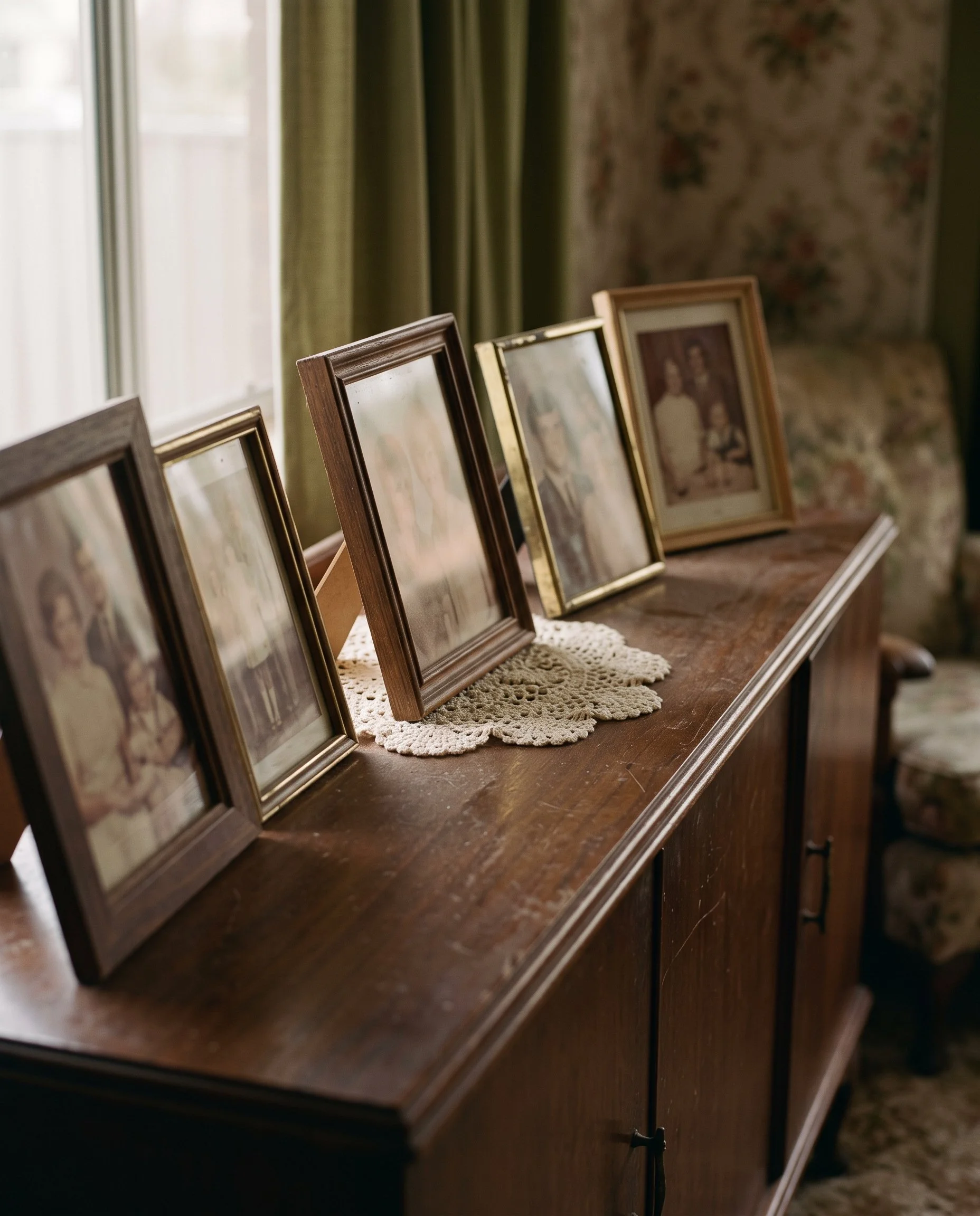 Framed family photographs arranged on a wooden sideboard beside a window