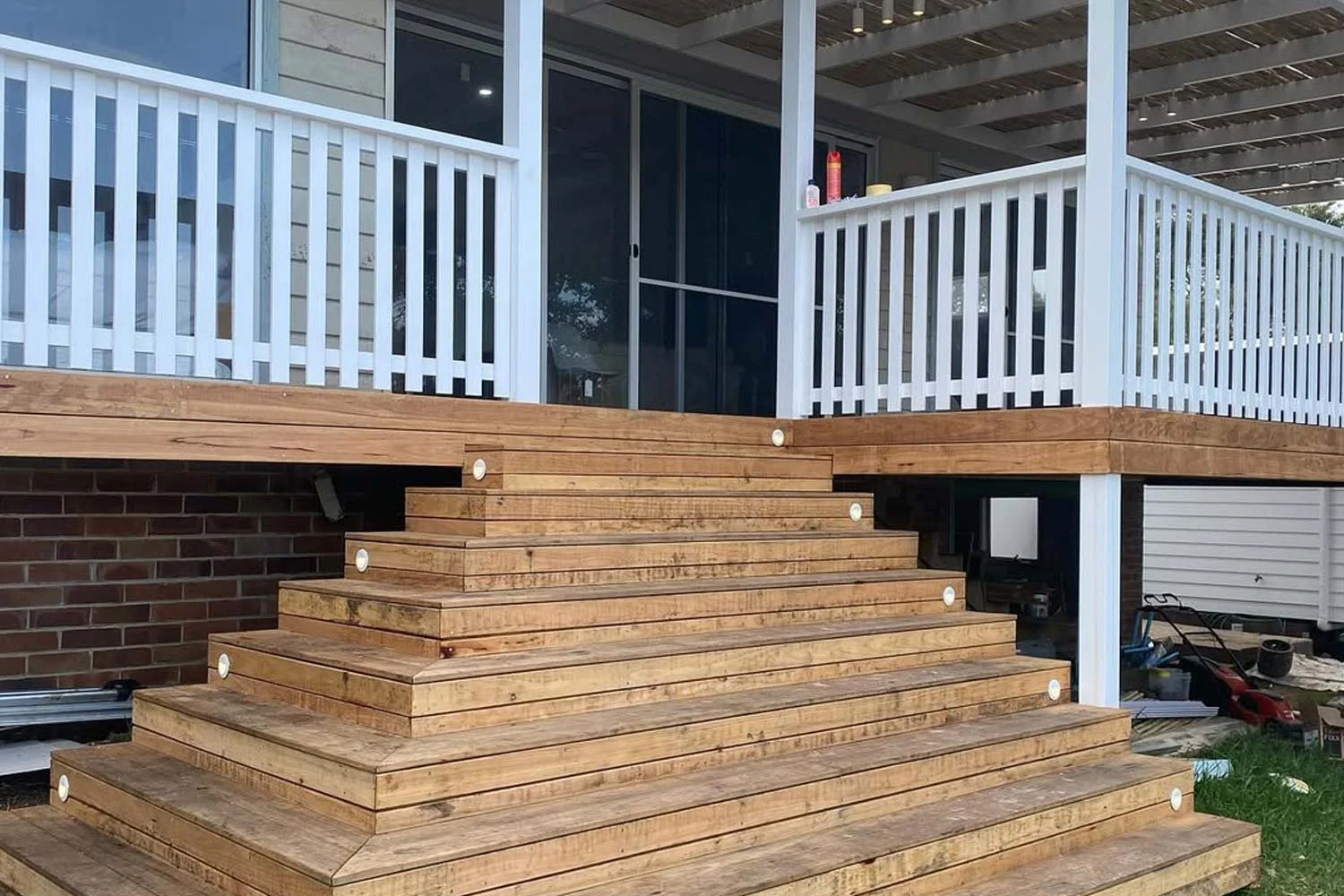 Wooden deck with white railings and wide steps leading up to a sliding glass door.