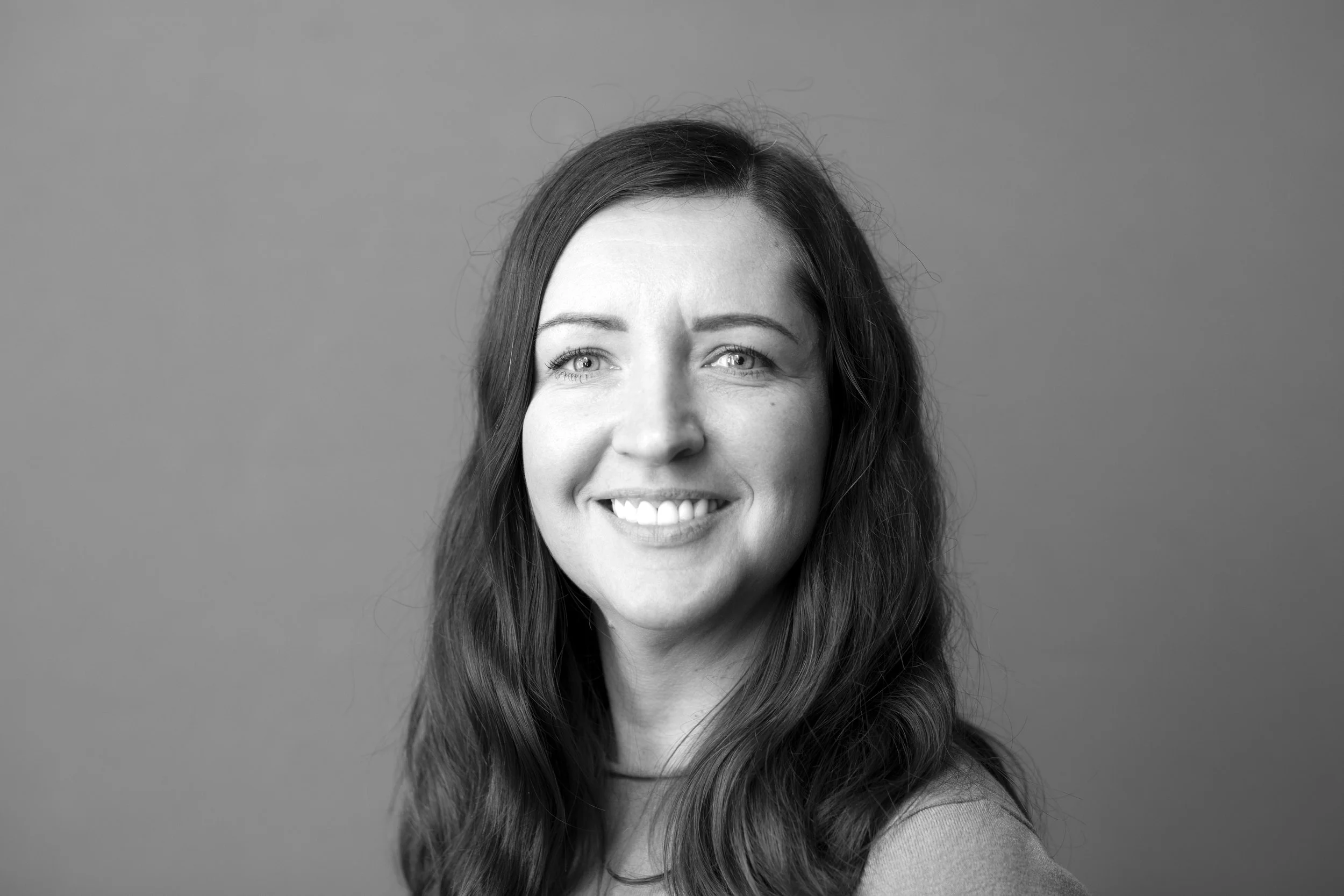Sort-hvid portræt af en smilende kvinde med langt, bølget hår, set mod en ensfarvet baggrund.