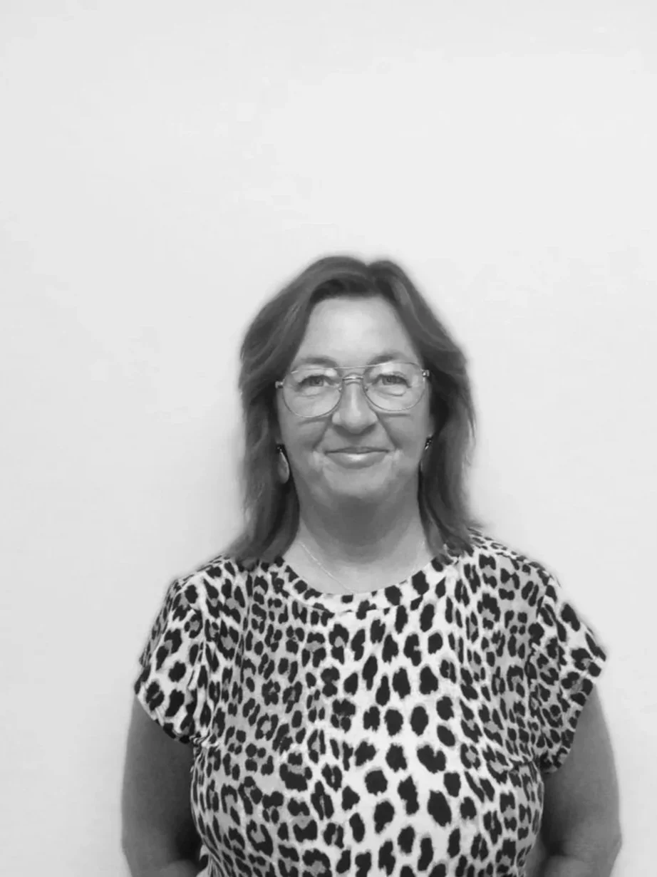 En kvinde med brunt, mellemlangt hår og briller, iført en leopardmønstret bluse, står foran en hvid væg.