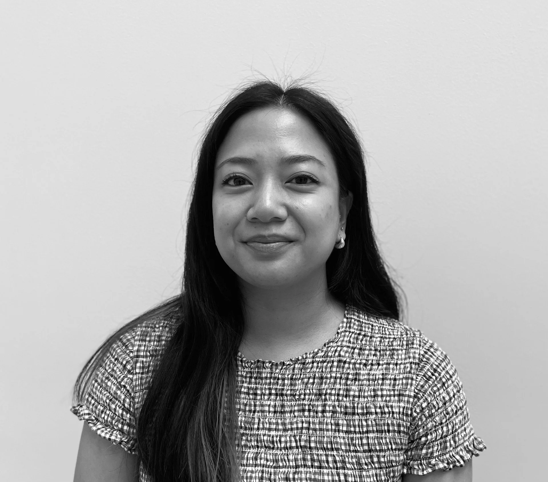 Sort-hvid portrætbillede af en smilende kvinde med mørkt, langt hår, iført en mønstrede ærmeløse bluse, mod en enkel baggrund.