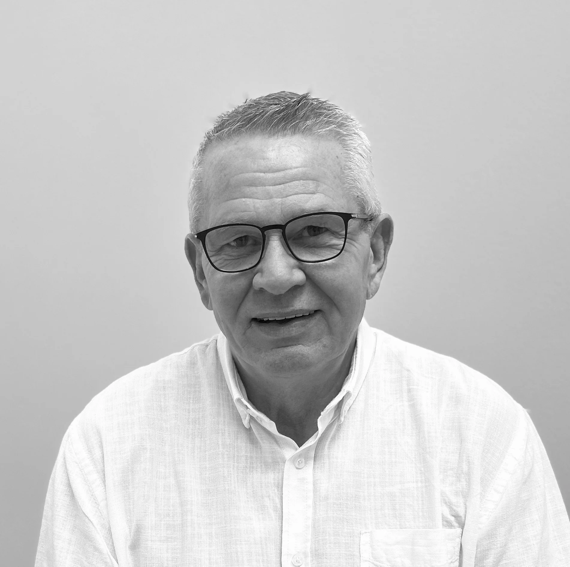 Sort-hvid portræt af en mand med briller, kort gråt hår og hvid skjorte, smilende og kiggende mod kameraet.