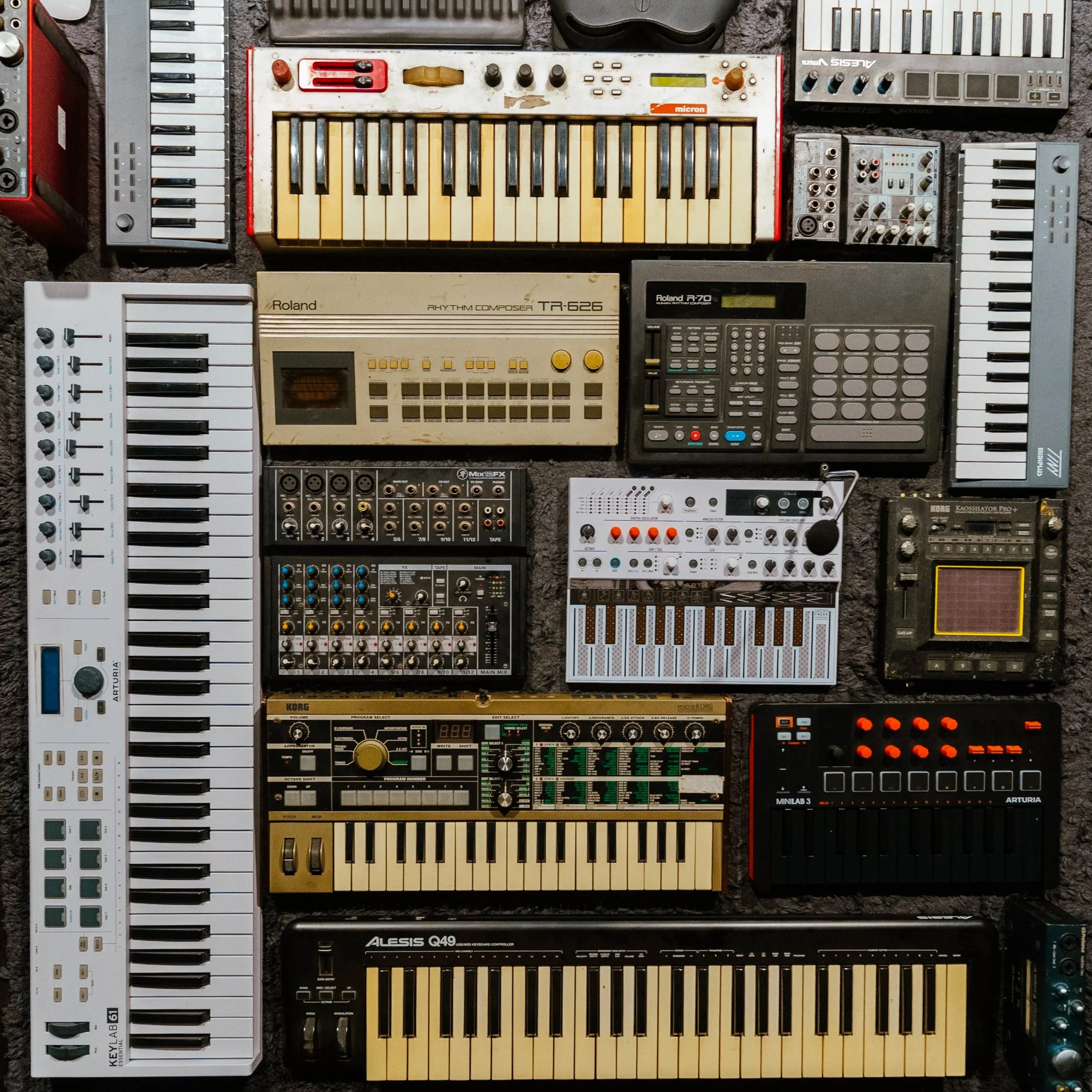 A collection of vintage and modern electronic music equipment, including synthesizers, drum machines, and audio controllers.