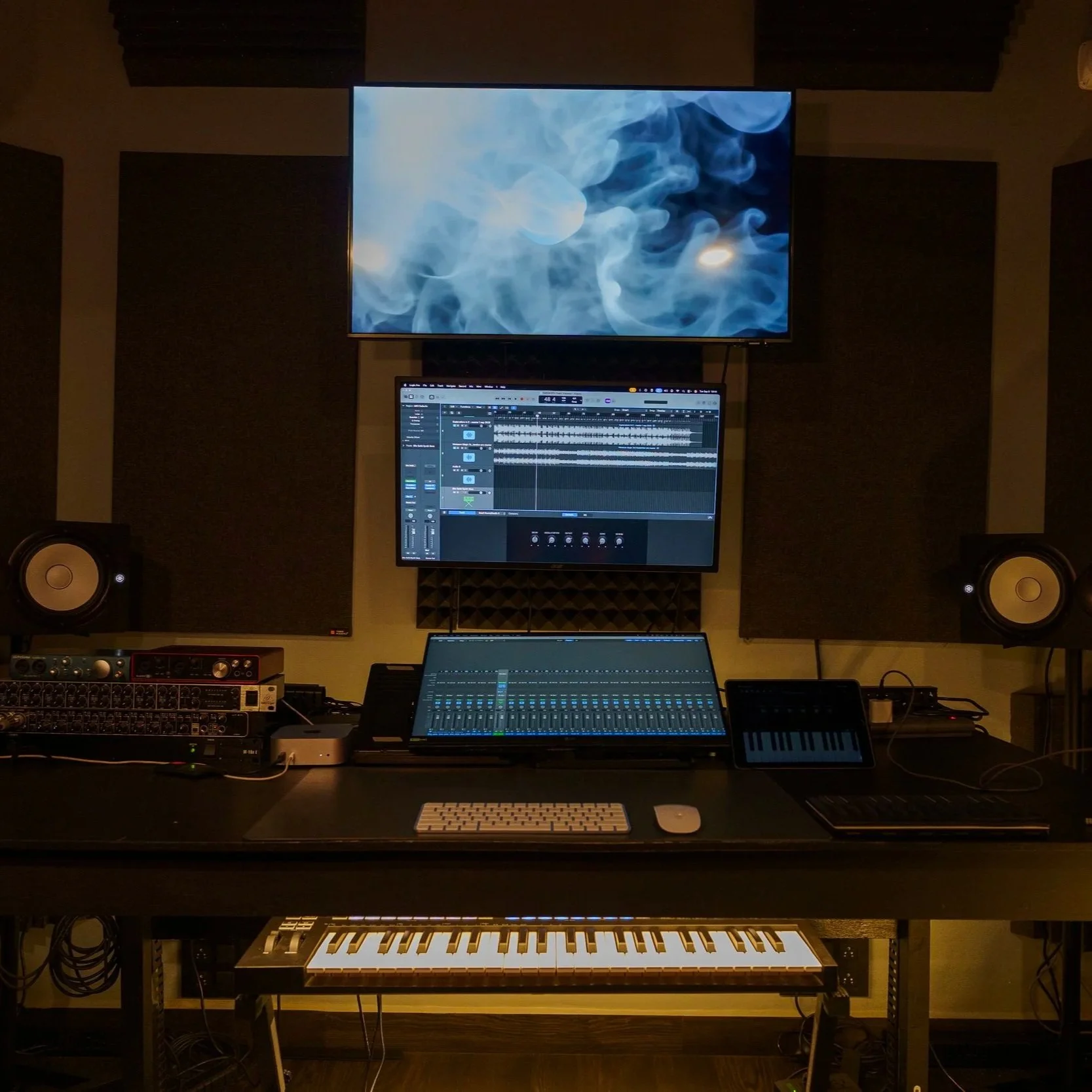 Music production studio setup with multiple monitors, speakers, keyboard, and audio equipment.