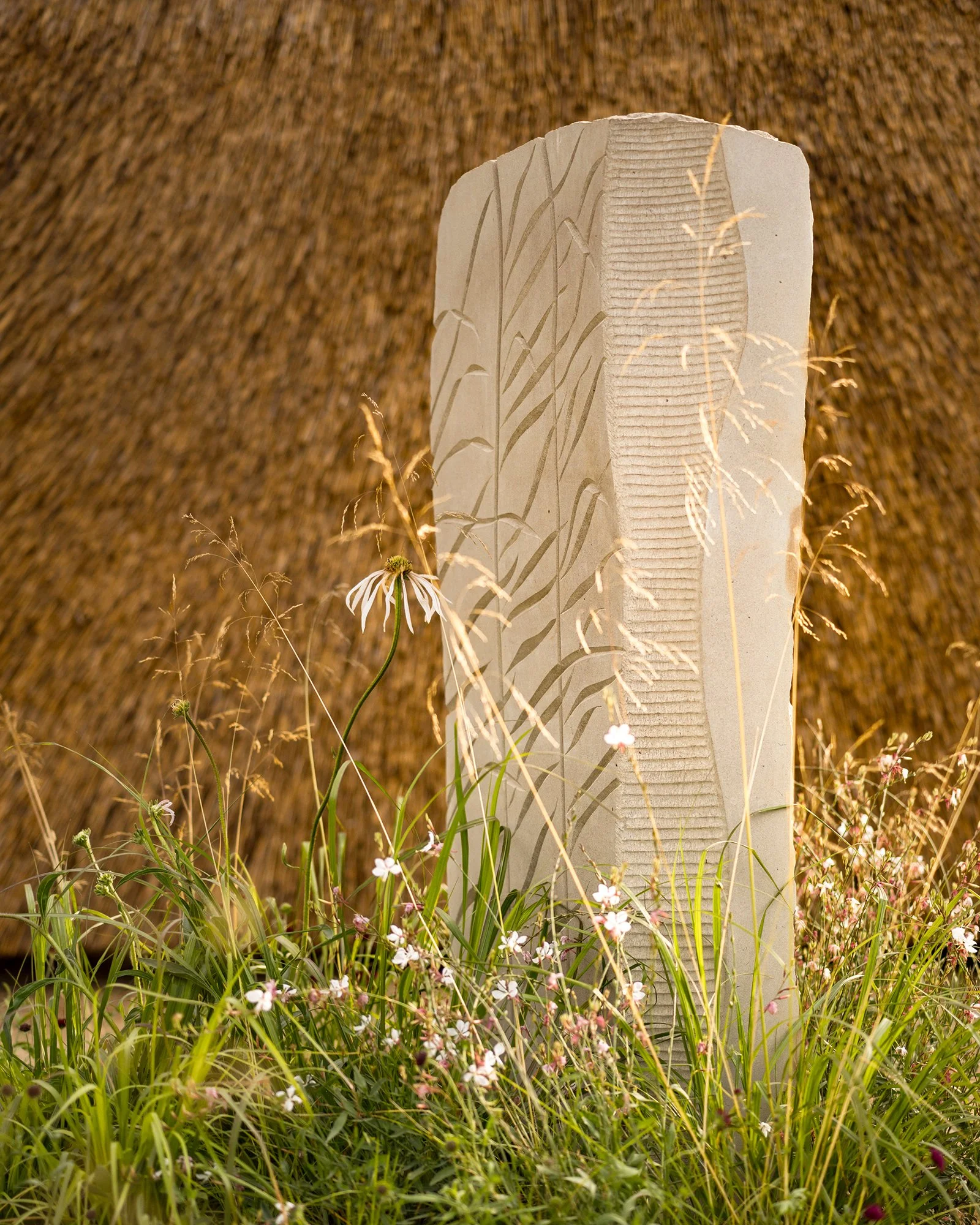 RHS Crafted from Nature Garden by Stark Strand. Image shows naturalistic planting inspired by Norfolk meadows and reed inspired York Stone sculpture by Teucer Wilson
