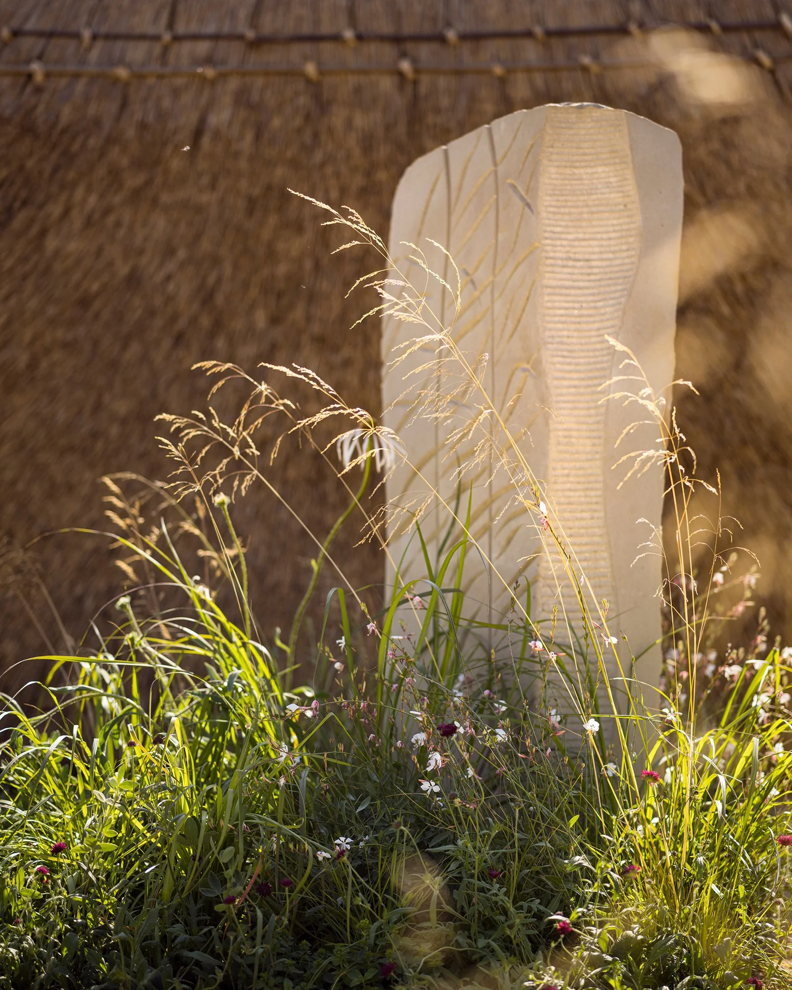RHS Crafted from Nature Garden by Stark Strand. Image shows naturalistic planting inspired by Norfolk meadows and reed inspired York Stone sculpture by Teucer Wilson