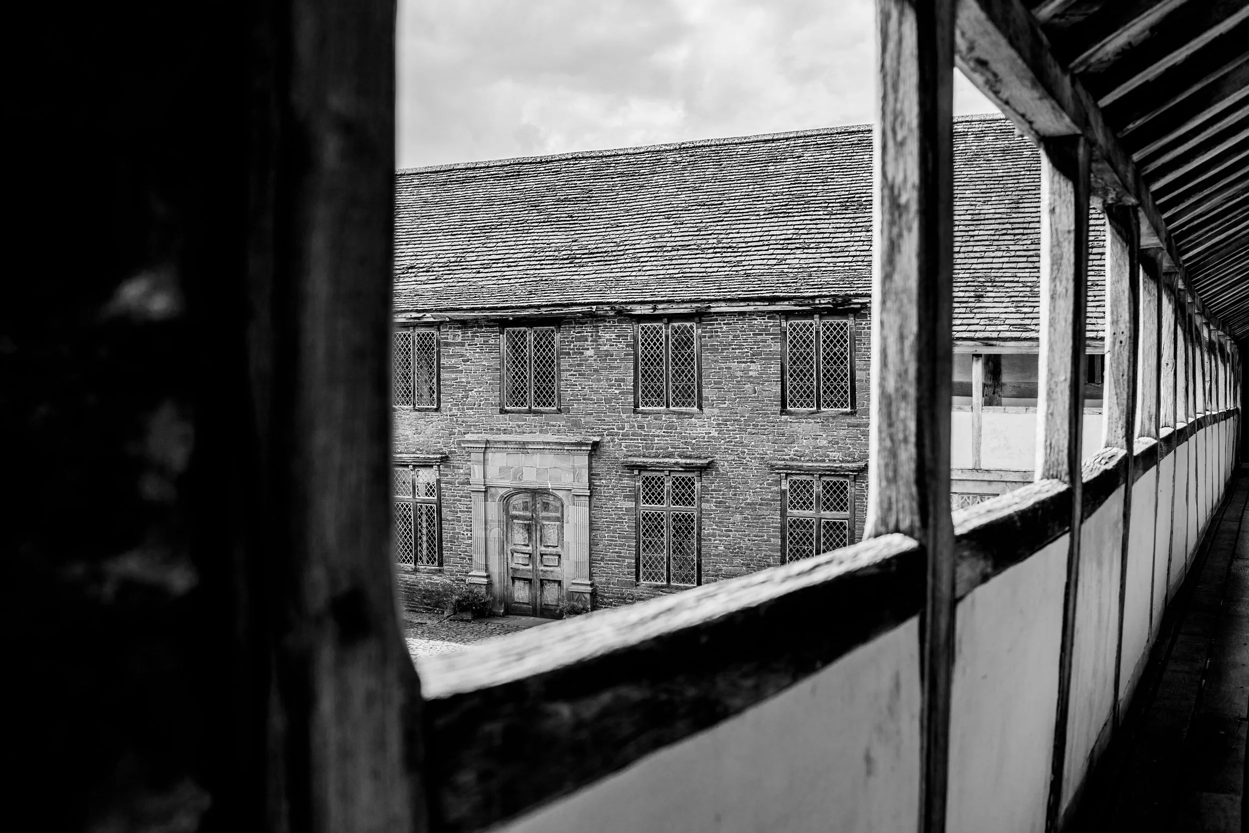 View of an old brick building with barred windows from behind a wooden fence, in black and white.