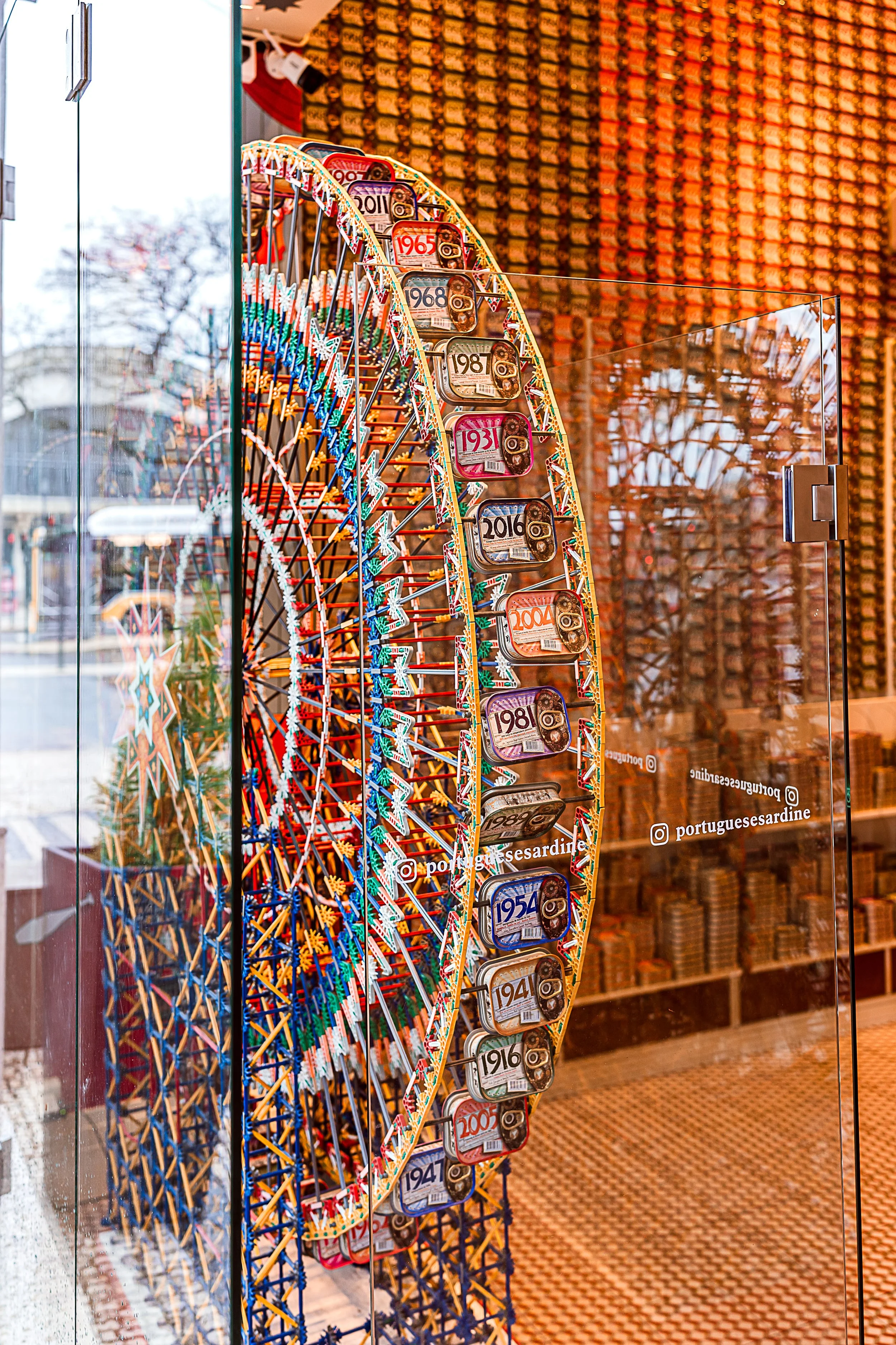 A colorful Ferris wheel display with vintage license plates from various years, enclosed in a glass case at a store called Portuguese Sardine.