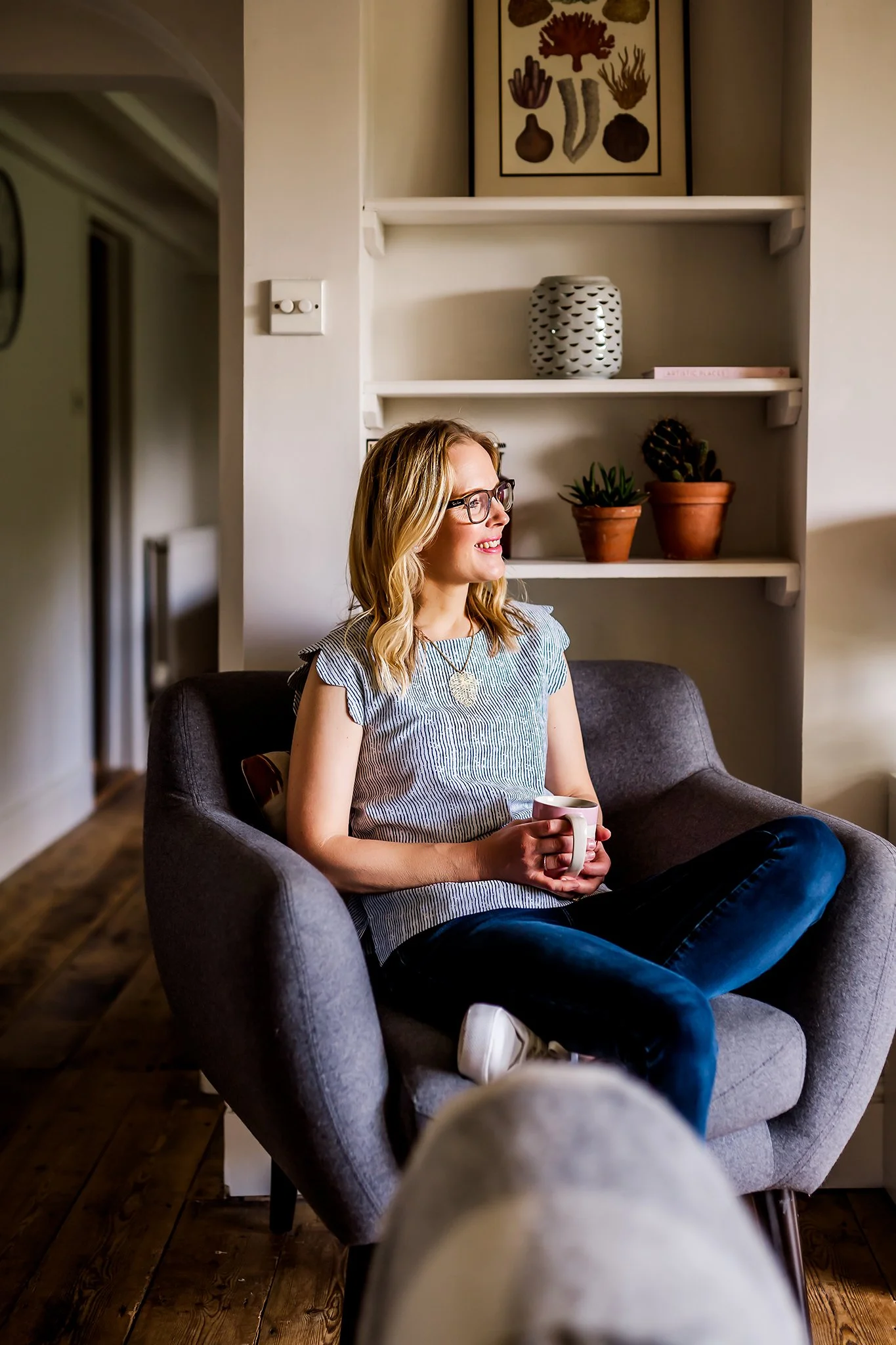 Social media manager, Kate, sits on a chair with a cup of tea in hand and gazes out the window during her branding photoshoot in Malvern