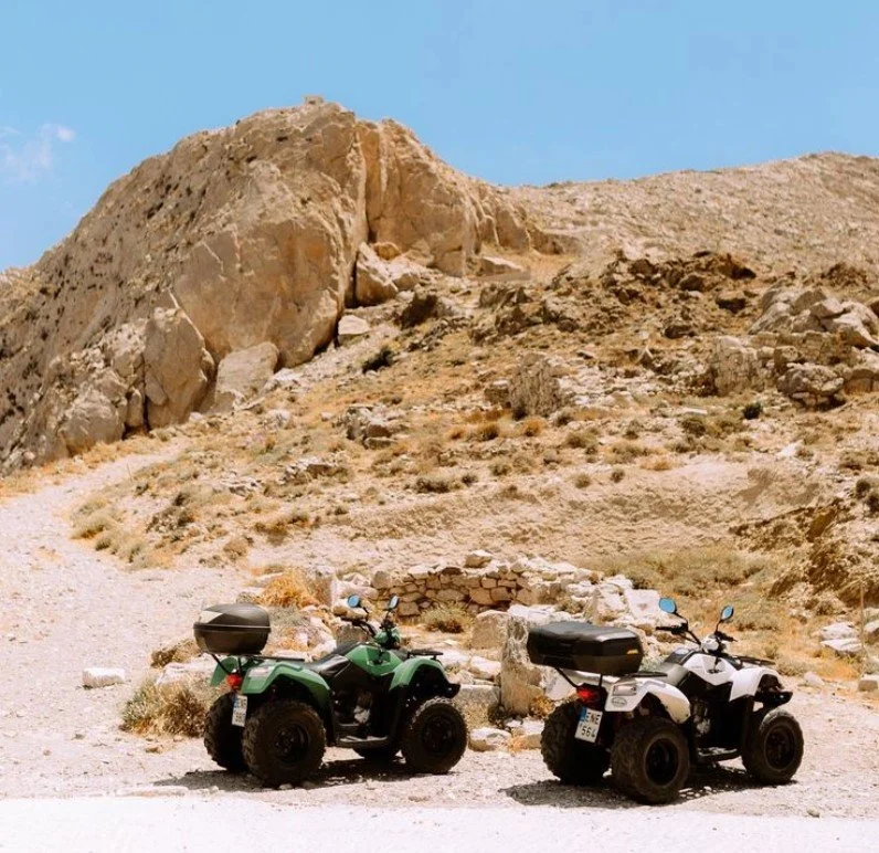 Two all-terrain vehicles (ATVs) parked in a rocky desert landscape with a clear blue sky.