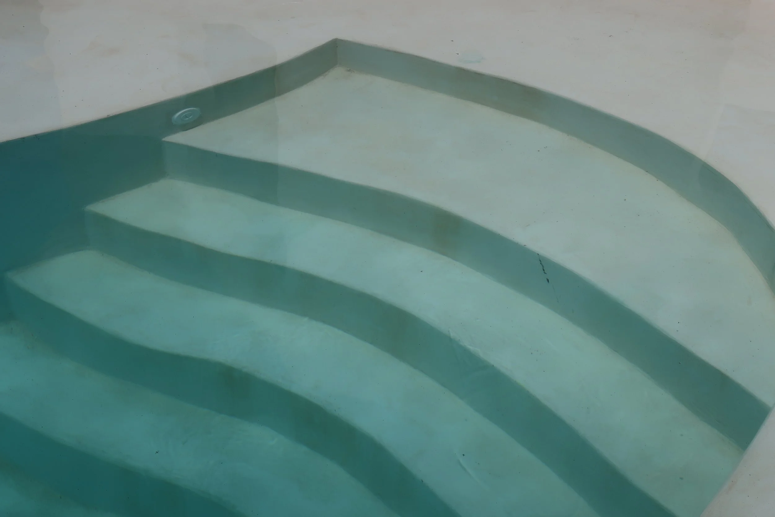 Close-up of a curved swimming pool staircase submerged in clear water.