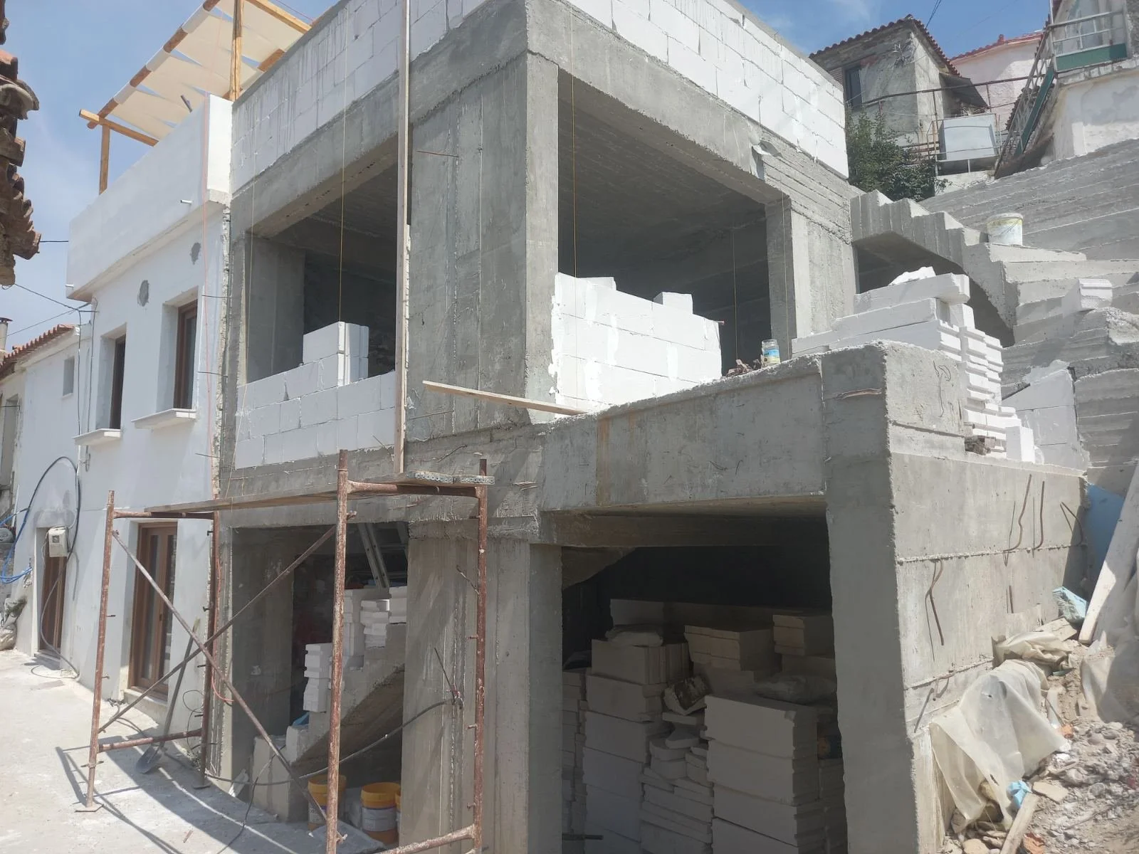 Construction site of a multi-story building with concrete and white bricks partially built, scaffolding on the front, and construction materials scattered around.