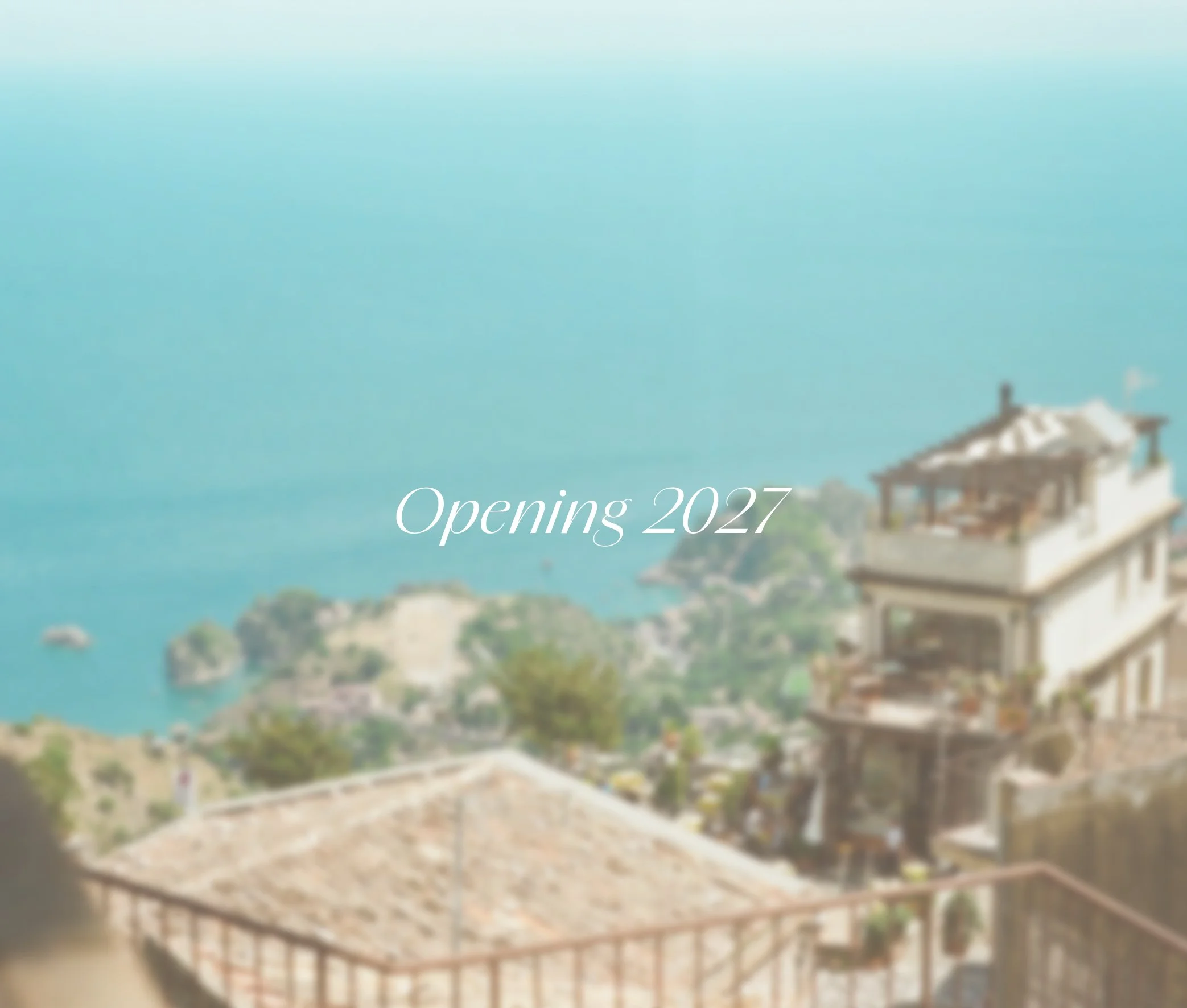 Blurred view of a seaside landscape with a building on the right, and the text 'Opening 2027' in the center. Samos Untold