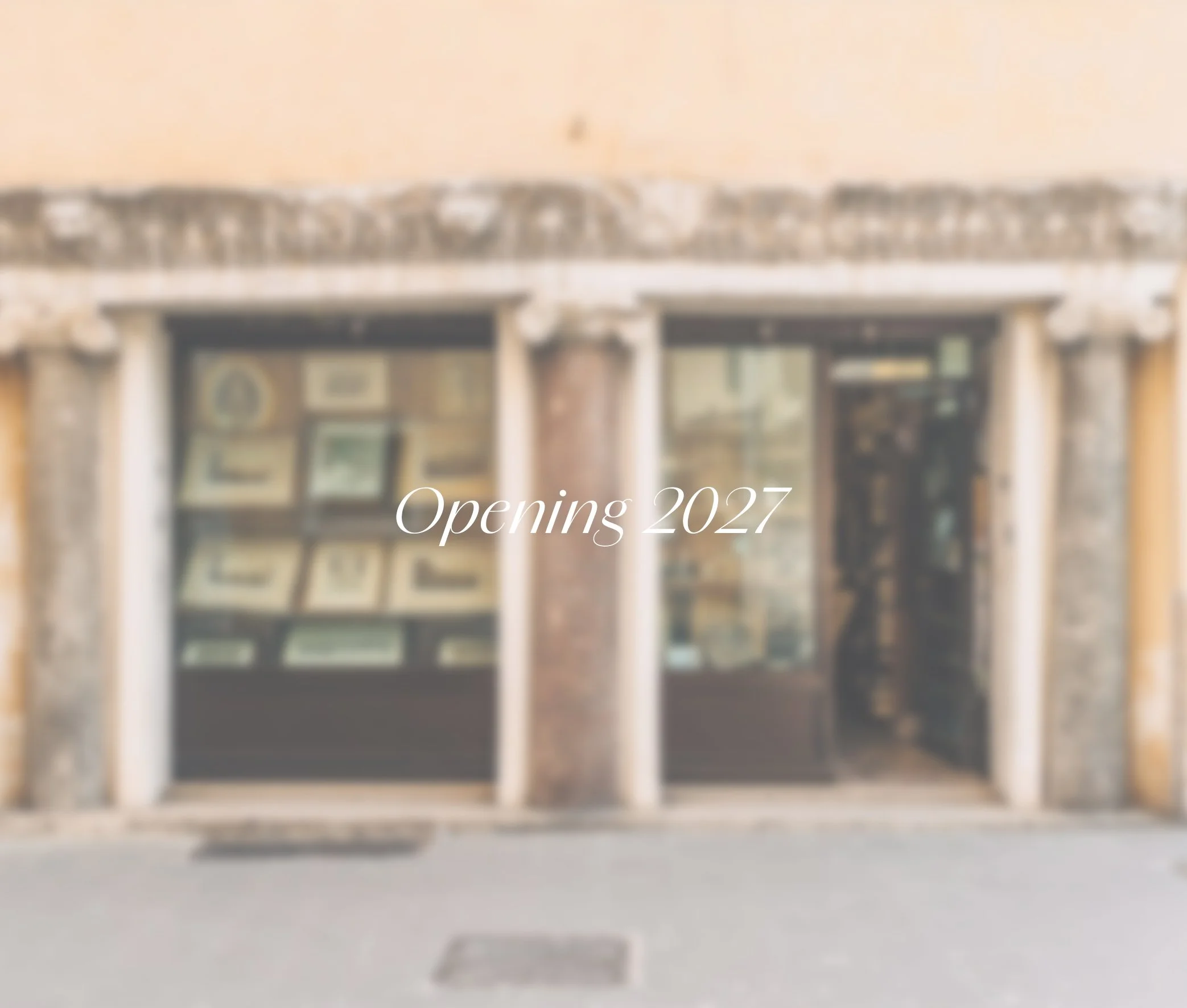 Blurry storefront with the text 'Opening 2027' overlaid, suggesting an upcoming business opening at Samos Untold