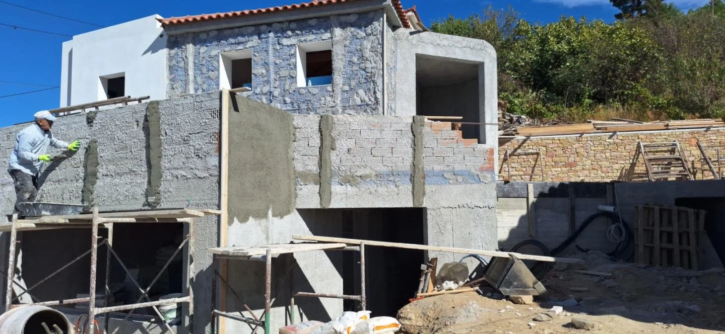 Construction worker applying plaster to a concrete wall of a building under construction on a sunny day.