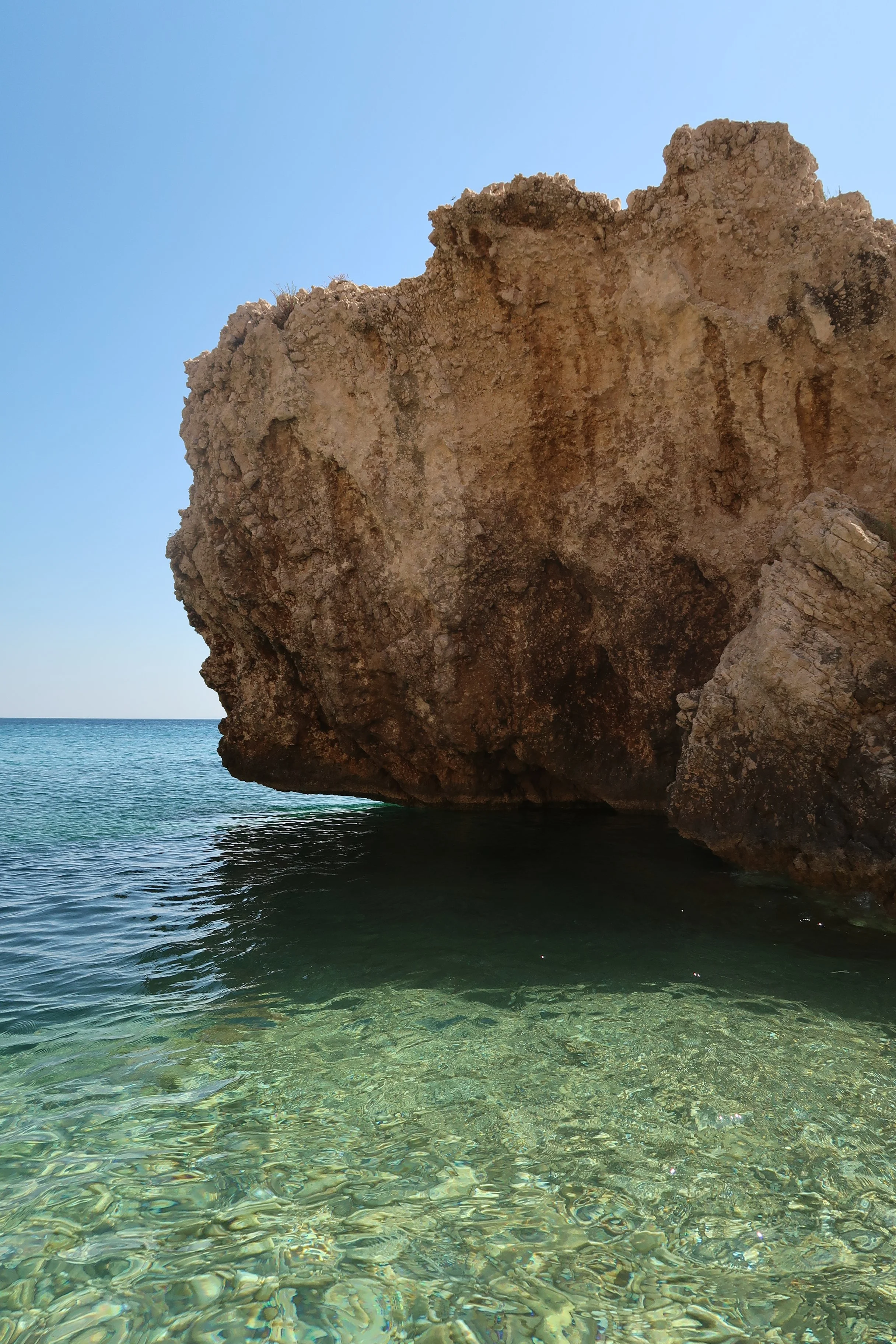 Large rock formation over clear ocean water on a sunny day.