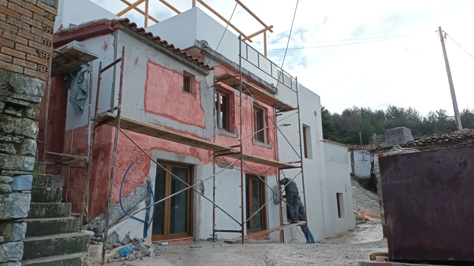 Construction of a white building with scaffolding, workers, and pink insulation or plaster on the exterior wall.