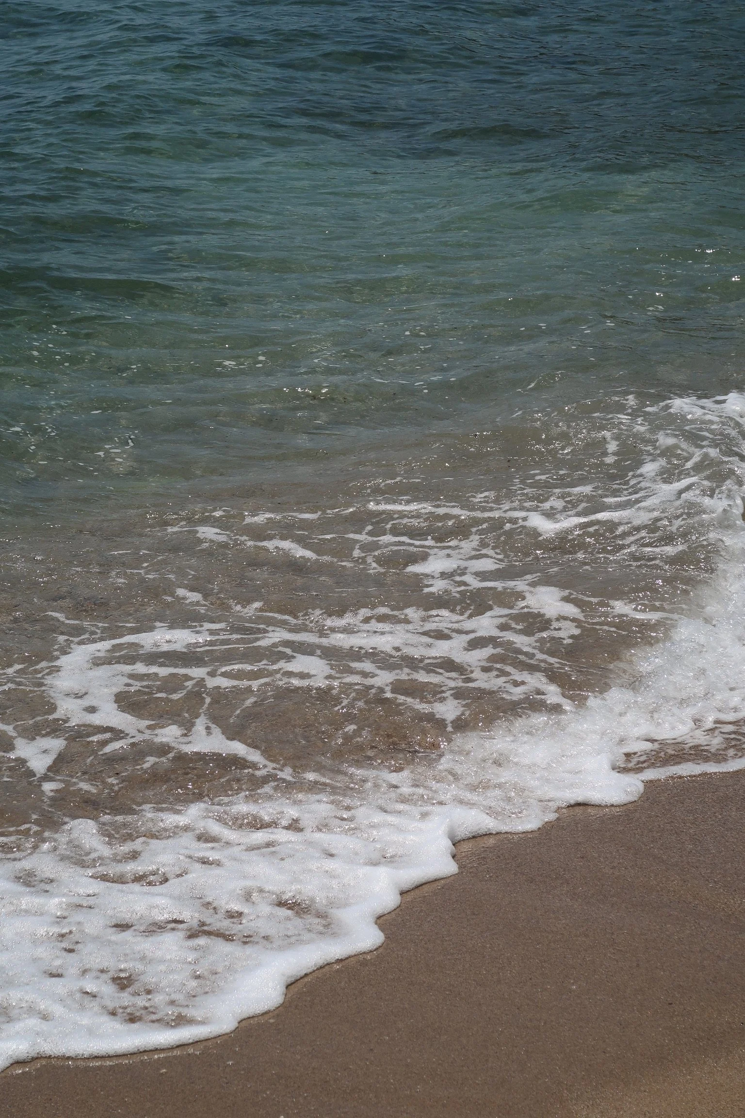 Photo of ocean waves gently hitting sandy beach shoreline.