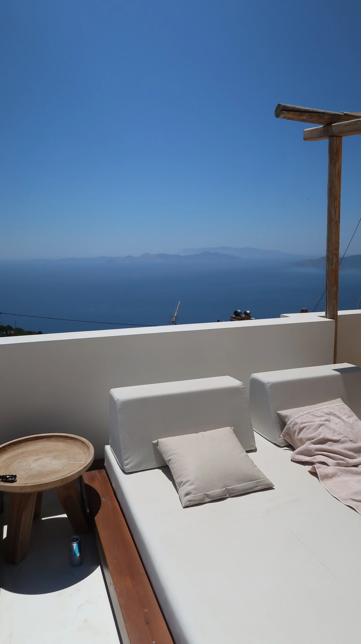 Outdoor terrace with a white daybed and cushions, overlooking a vast blue sea and distant mountains under a clear blue sky on Samos Untold