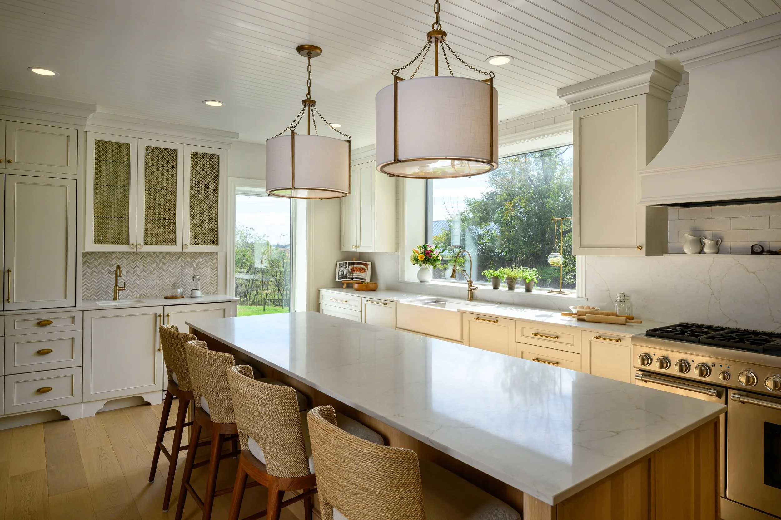 Bright kitchen with large island, white cabinets, brass hardware, and two large hanging pendant lights.
