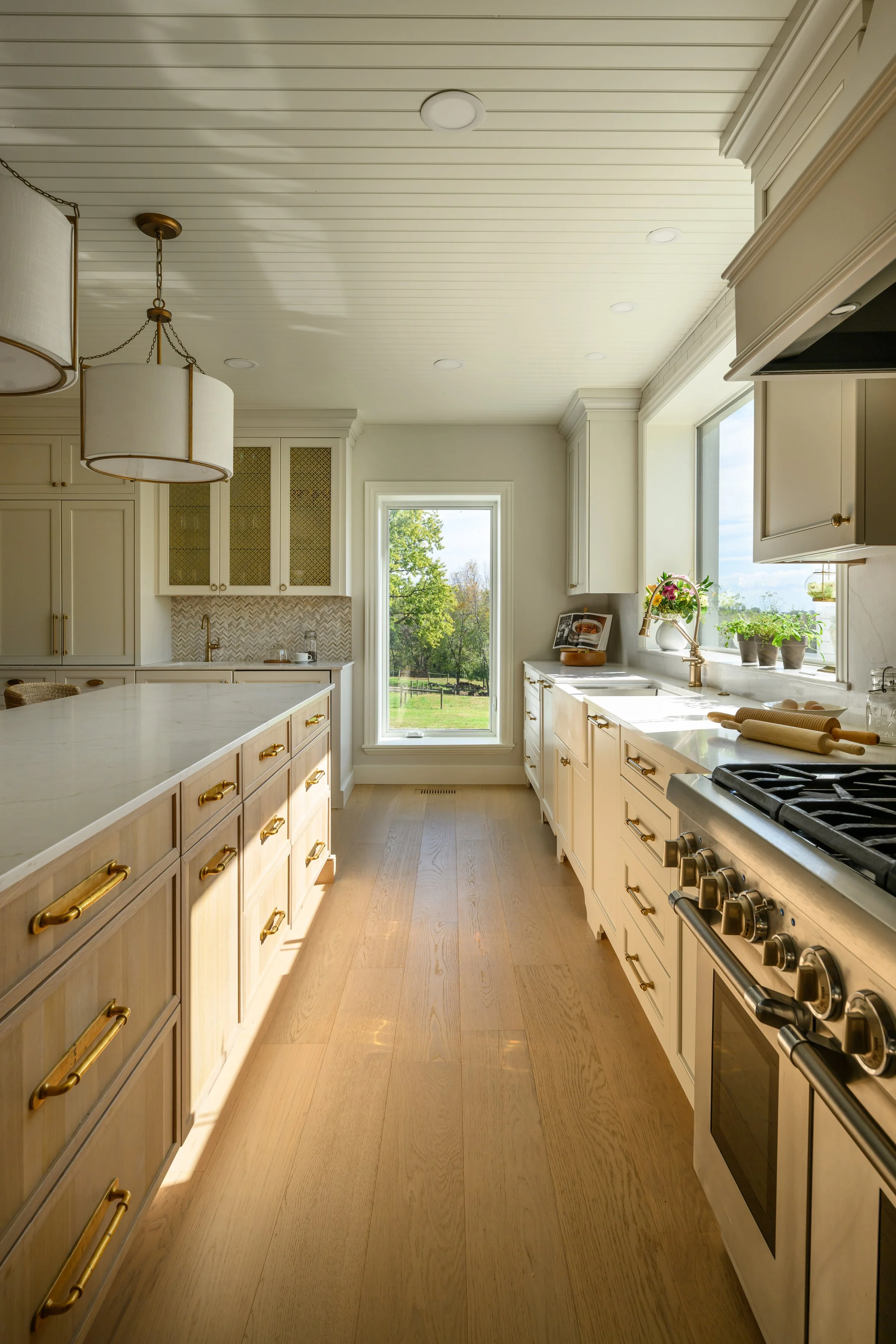 Bright kitchen with cream cabinets, a large island, and a view of a backyard through a window.