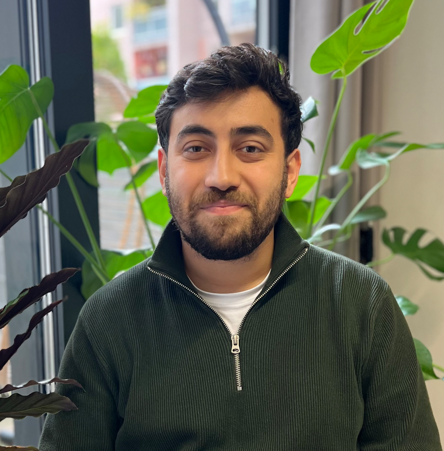 Ein Mann in einem dunkelblauen Pullover und einem gestreiften Hemd lächelt in die Kamera vor einem neutralen Hintergrund. Erfahrener Trainer der METASKILLS.academy