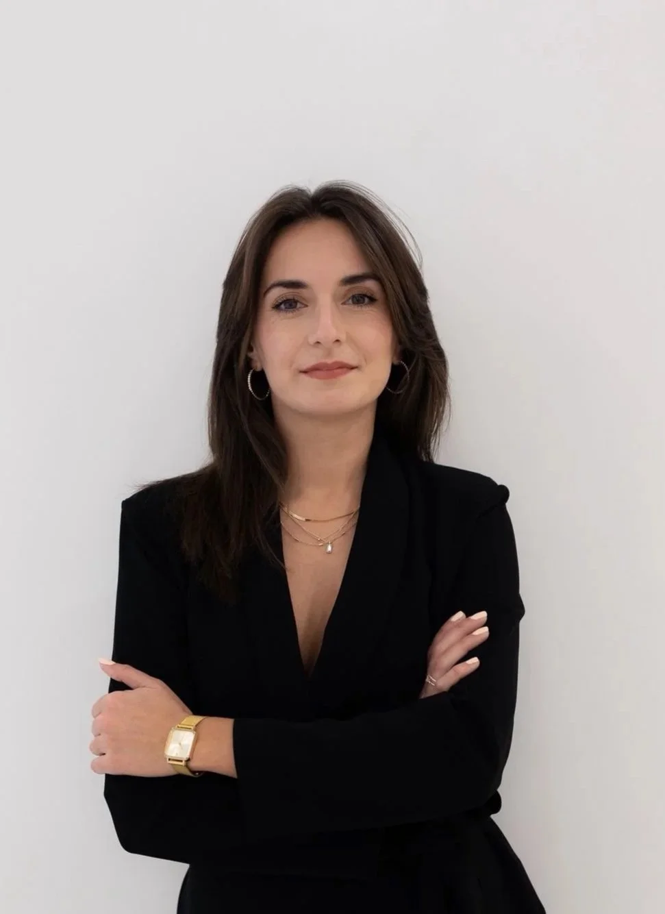 Frau mit langen Haaren trägt ein schwarzes Top vor einem weißen Hintergrund.