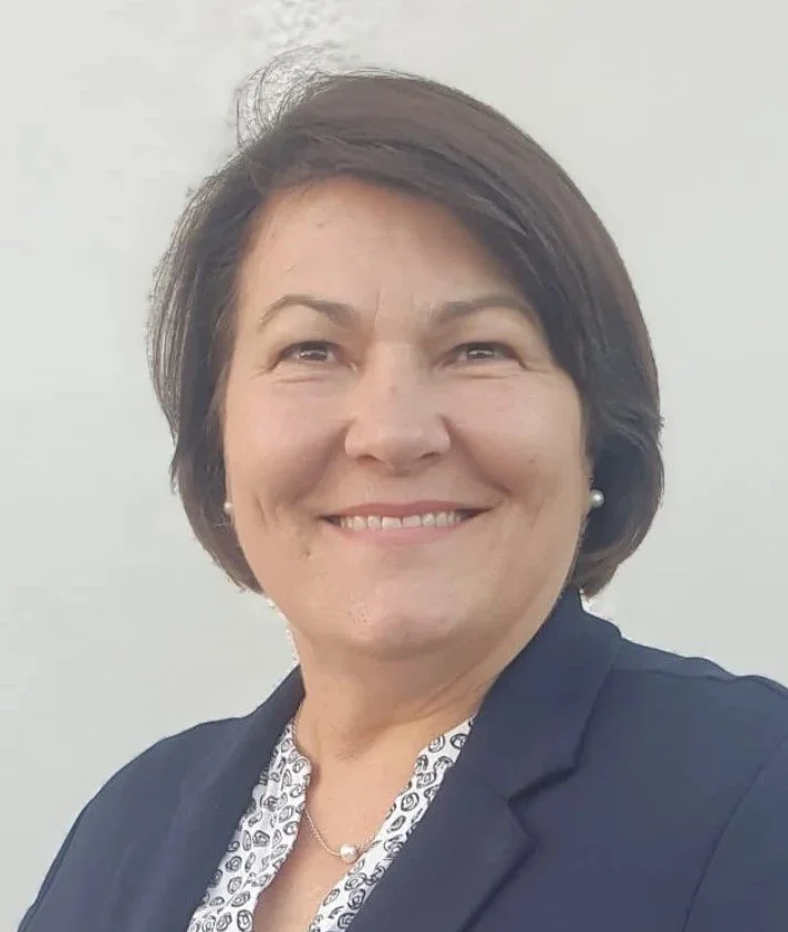 Frau im blauen Jeansjacke steht vor grünen Bäumen.