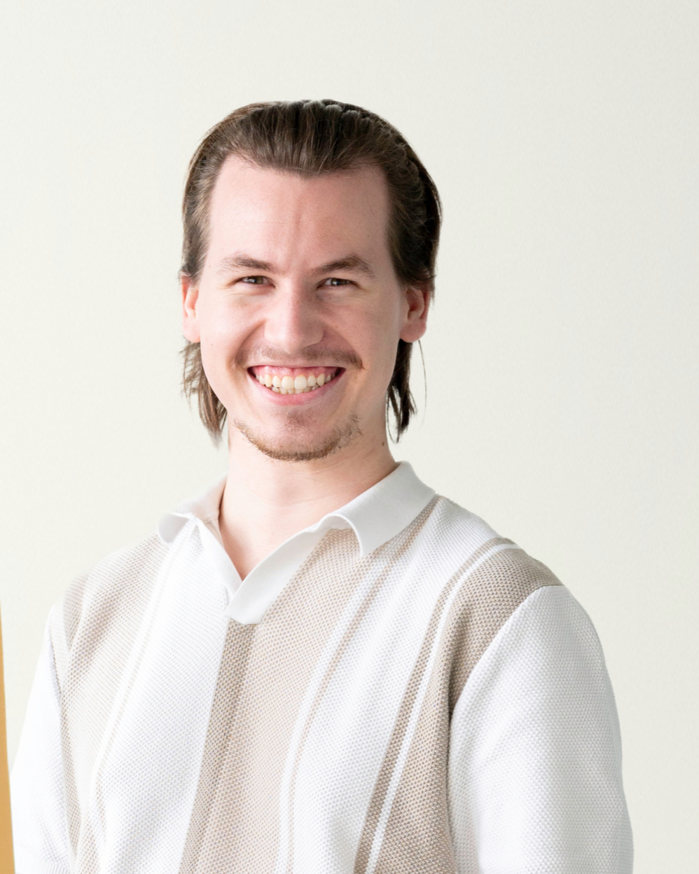 Lächelnder Mann im Freien, trägt ein weißes Hemd, mit unscharfem Hintergrund aus grünen Pflanzen.