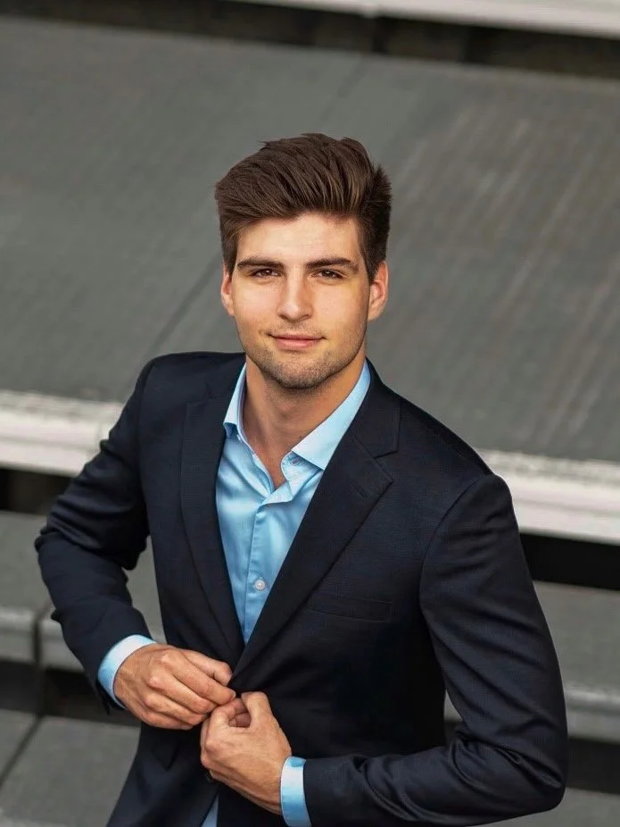 Ein Mann mit blauem Kapuzenpullover und Baseballmütze steht vor einem bewölkten Himmel.