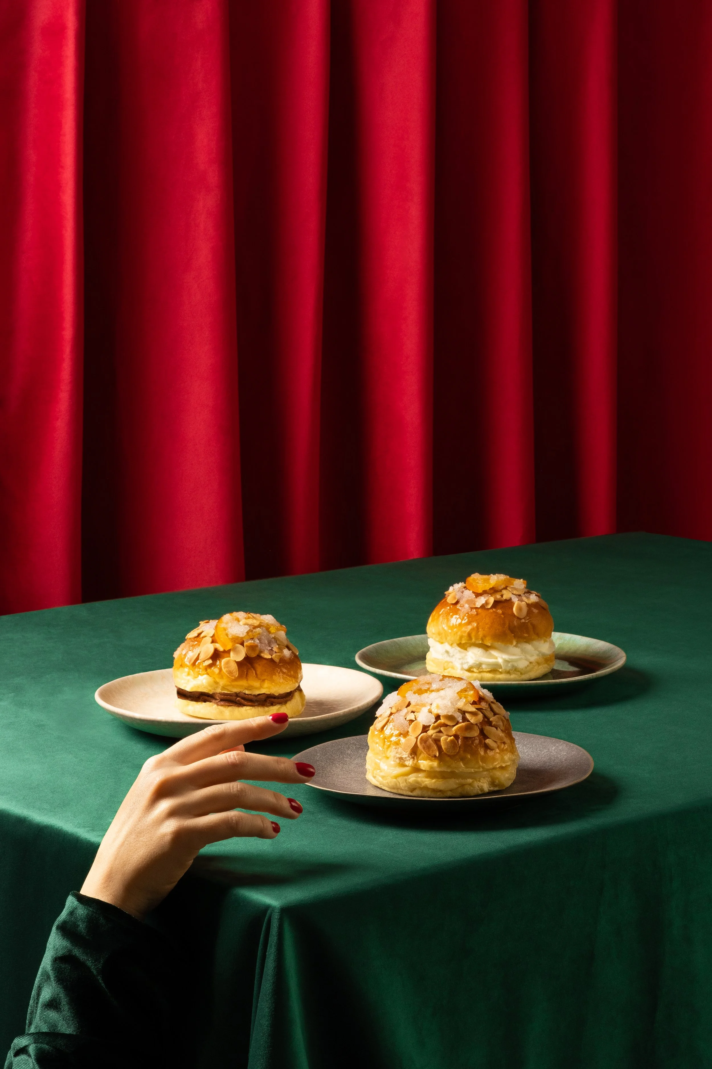 Tres platos con pastelitos en una mesa cubierta con tela verde, tras un telón rojo. Dirección creativa y fotografía de GustoStudio