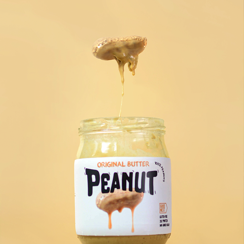 Vaso de vidrio con mantequilla de cacahuate que parece estar en proceso de ser servida, con un trozo de mantequilla suspendido en el aire. Diseño de packaging y dirección creativa y foto de GustoStudio.