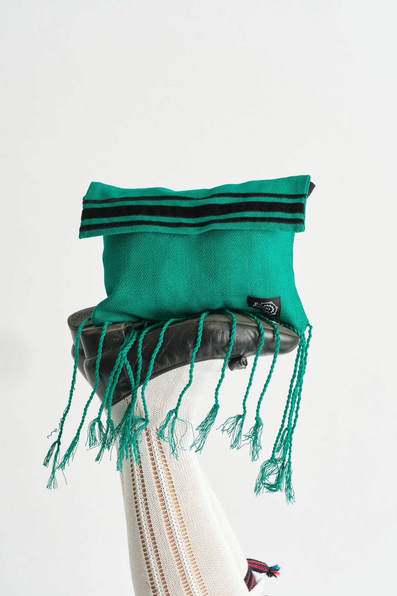 Sombrero negro sobre una pierna con medias blancas y calcetines de rayas, con una bolsa de tela verde en forma de paquete. Dirección creativa y foto por GustoStudio en Asturias