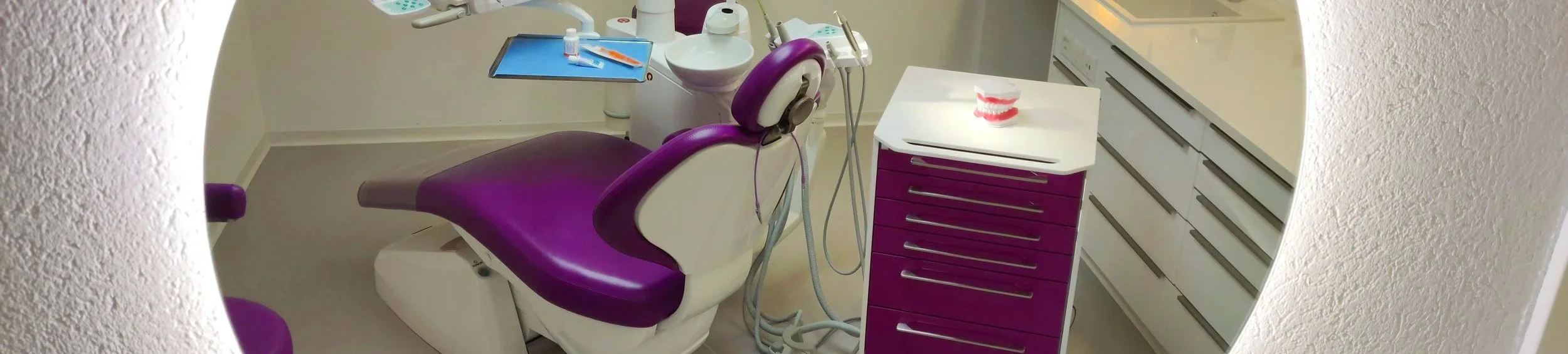 Eine Fotoaufnahme eines Behandlunszimmers. Im Zimmer befindet sich ei Zahnarztstuhl umgeben von diversem Equipment.