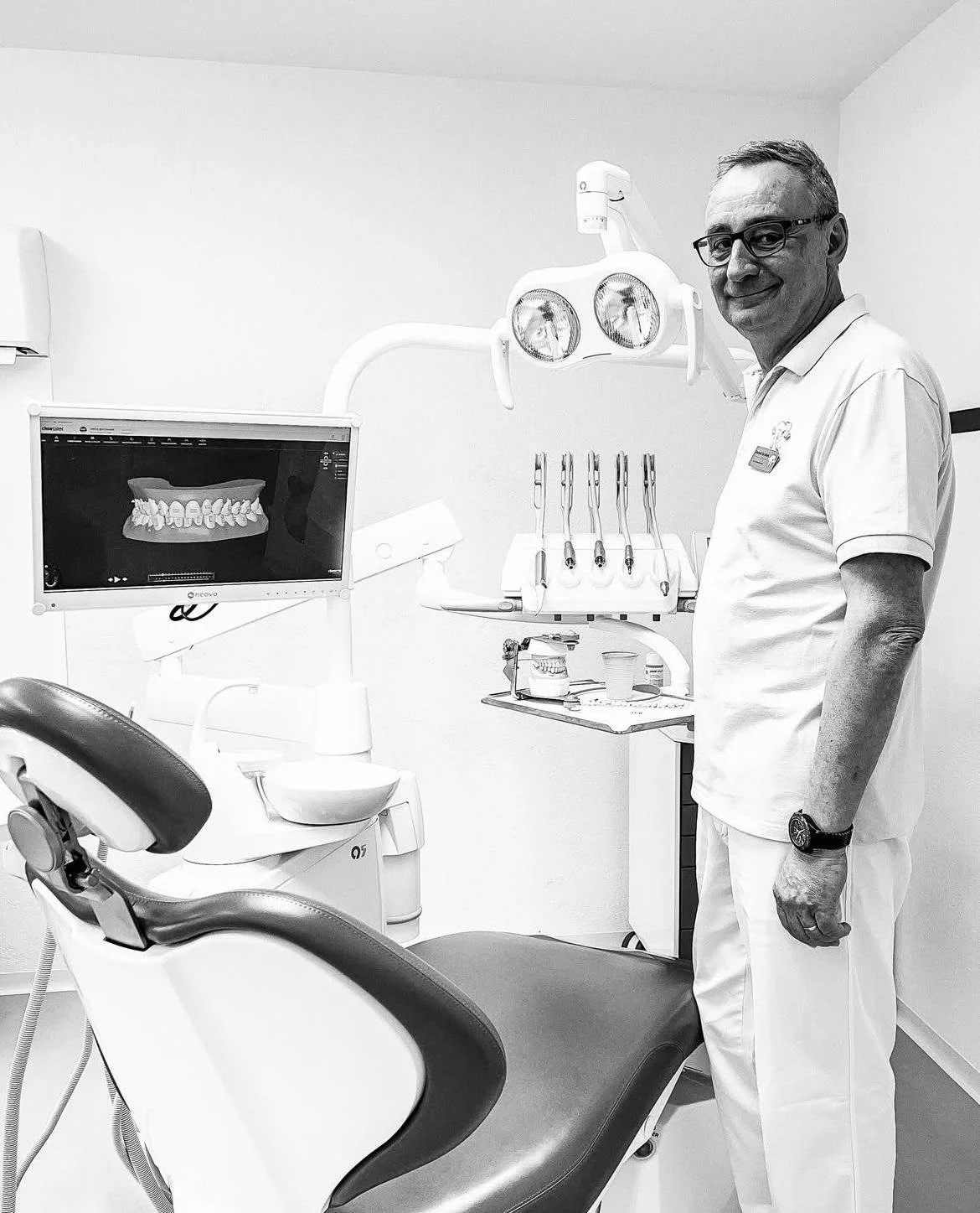 Zahnarzt im Behandlungsraum mit Zahnarztstuhl, Computerbildschirm mit Zahnmodell, und zahnärztlichen Instrumenten.