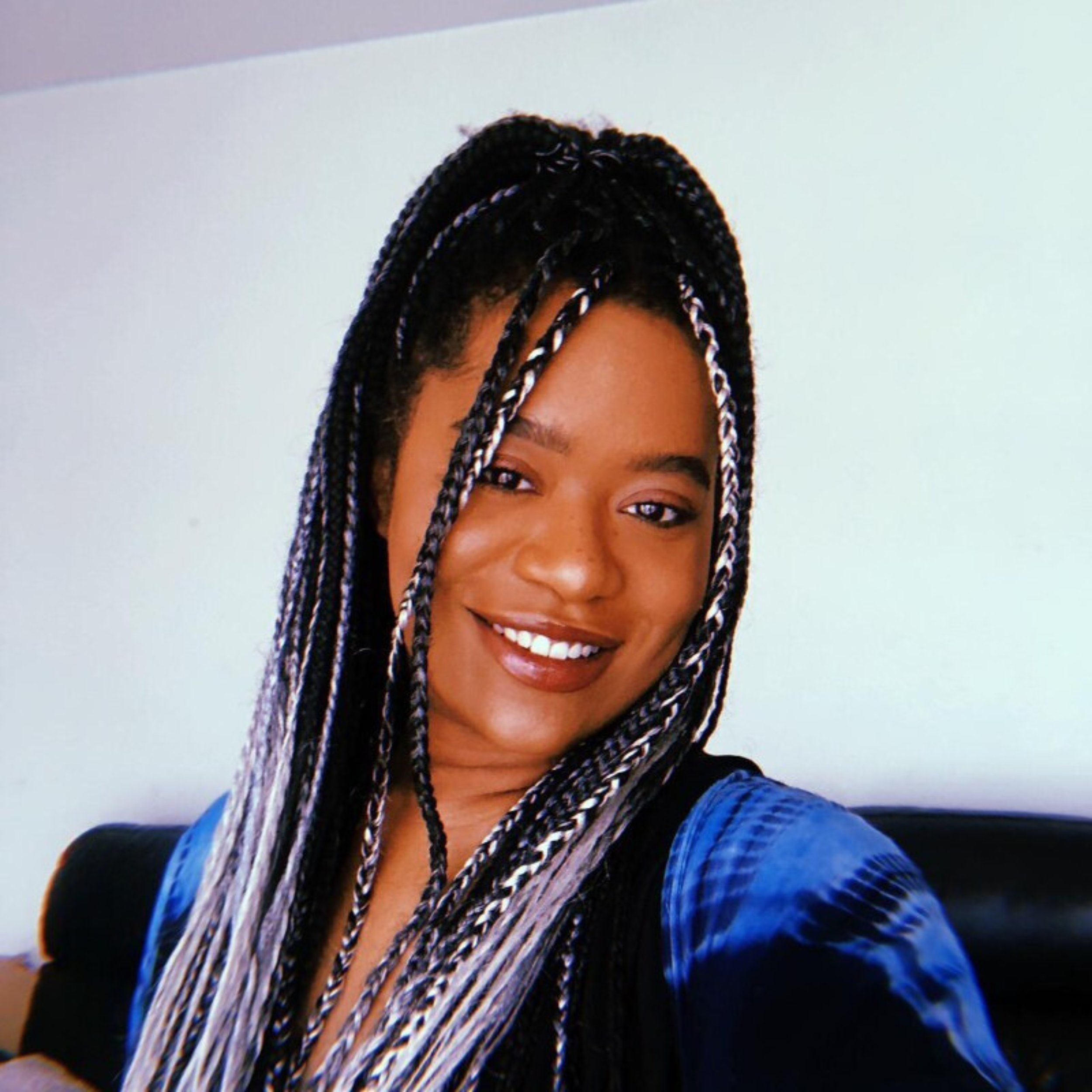 Smiling person with braided hair, wearing a blue shirt, against a light background.