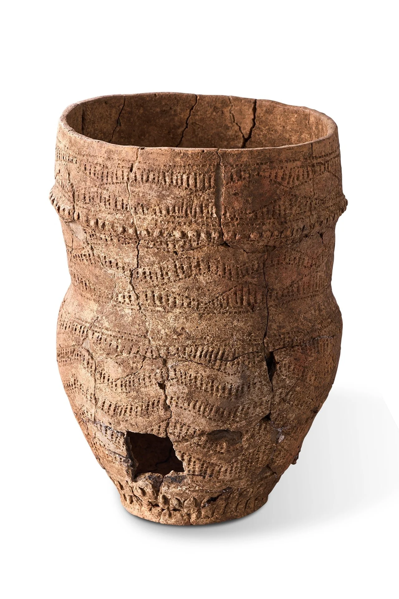 Ancient clay pot with decorative patterns and cracks, partially broken with a hole near the bottom.