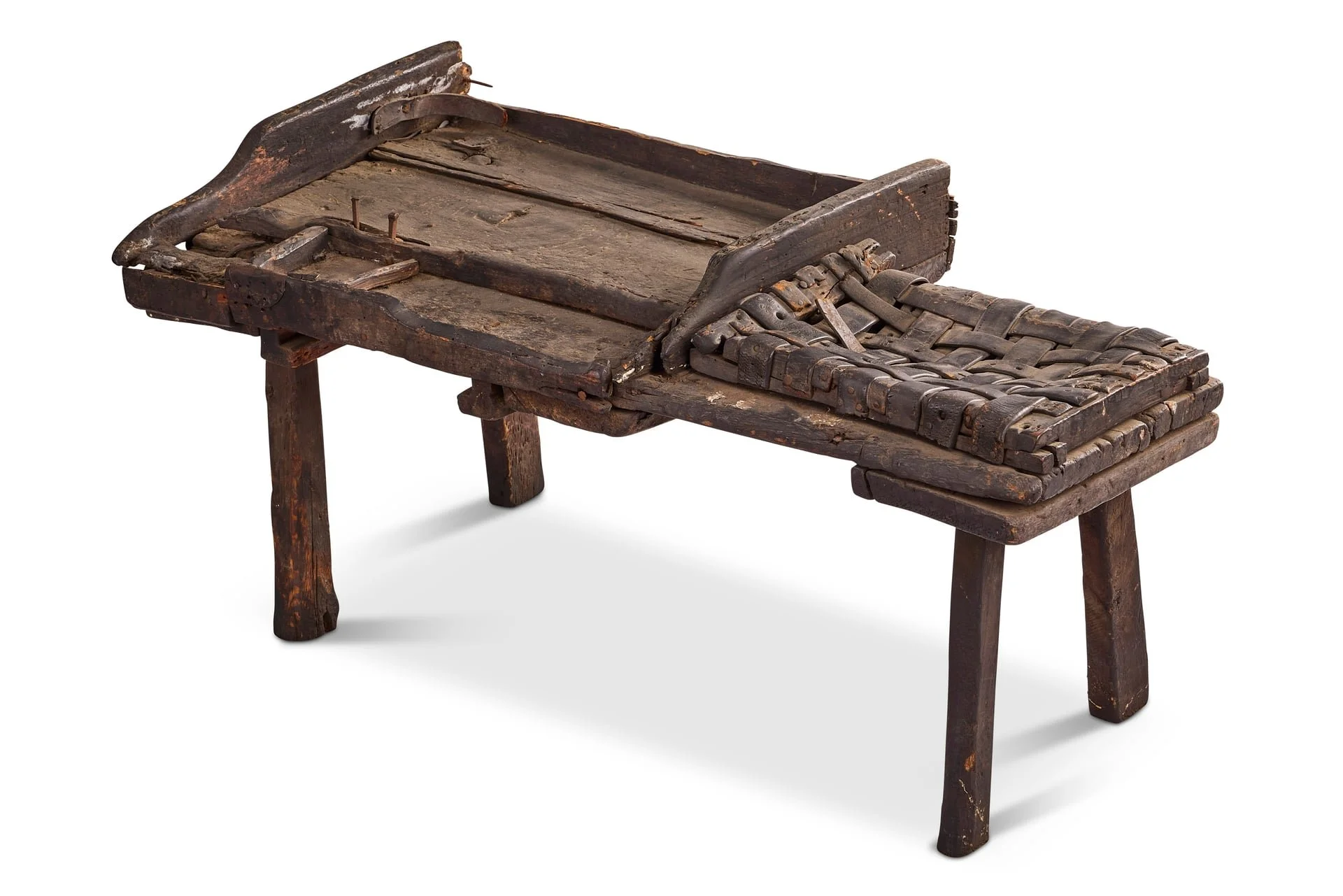 An old, rustic wooden stretcher or cot with a worn surface and leather straps, supported by four sturdy legs.