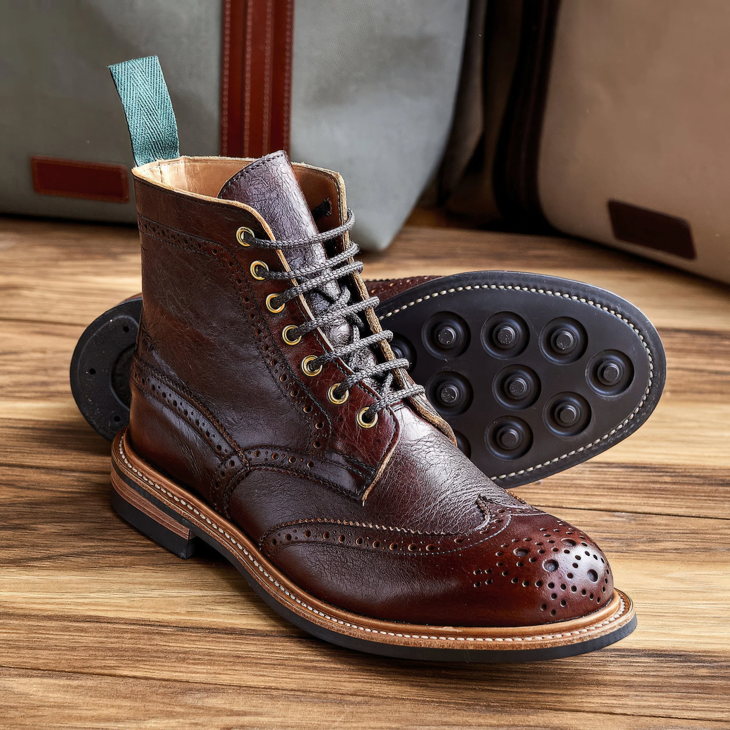 A close-up of a brown leather dress shoe with decorative perforations, resting on a wooden surface. In the background, a pair of gray and brown rollerblades are visible, along with a gray fabric bag with a red stripe and a teal loop.