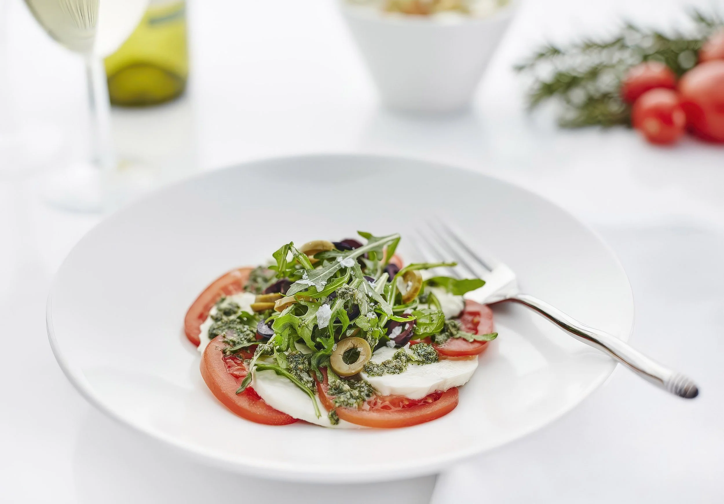 Caprese salad with sliced tomatoes, mozzarella, green herbs, and olive oil on a white plate