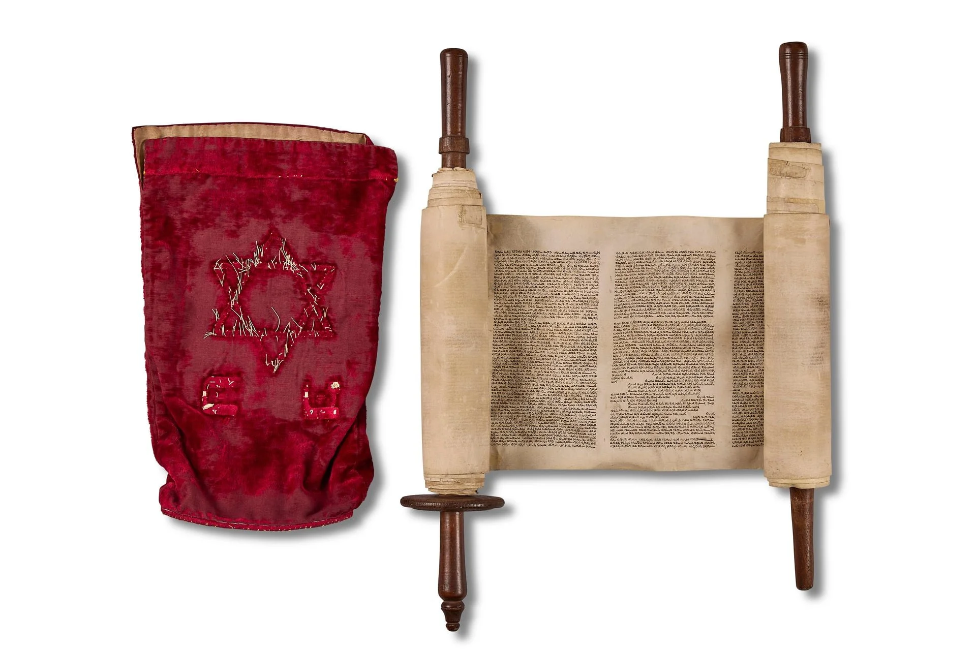 A tall red velvet bag with a sequined Star of David and chairs embroidered on it, placed next to an open scroll with Hebrew text.