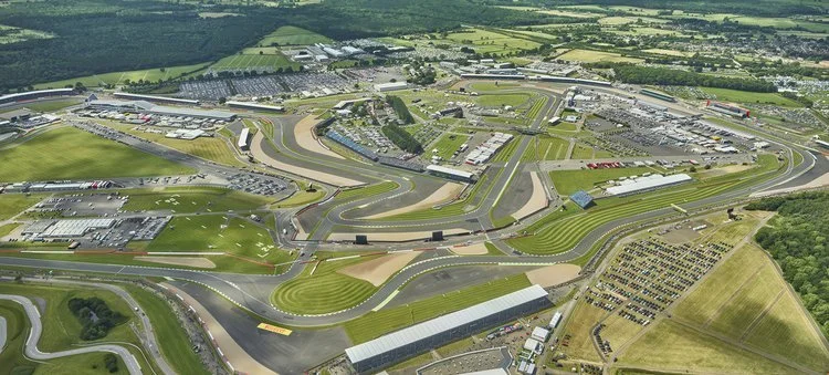 Aerial view of a race track with multiple turns, grandstands, and surrounding facilities, surrounded by green fields.