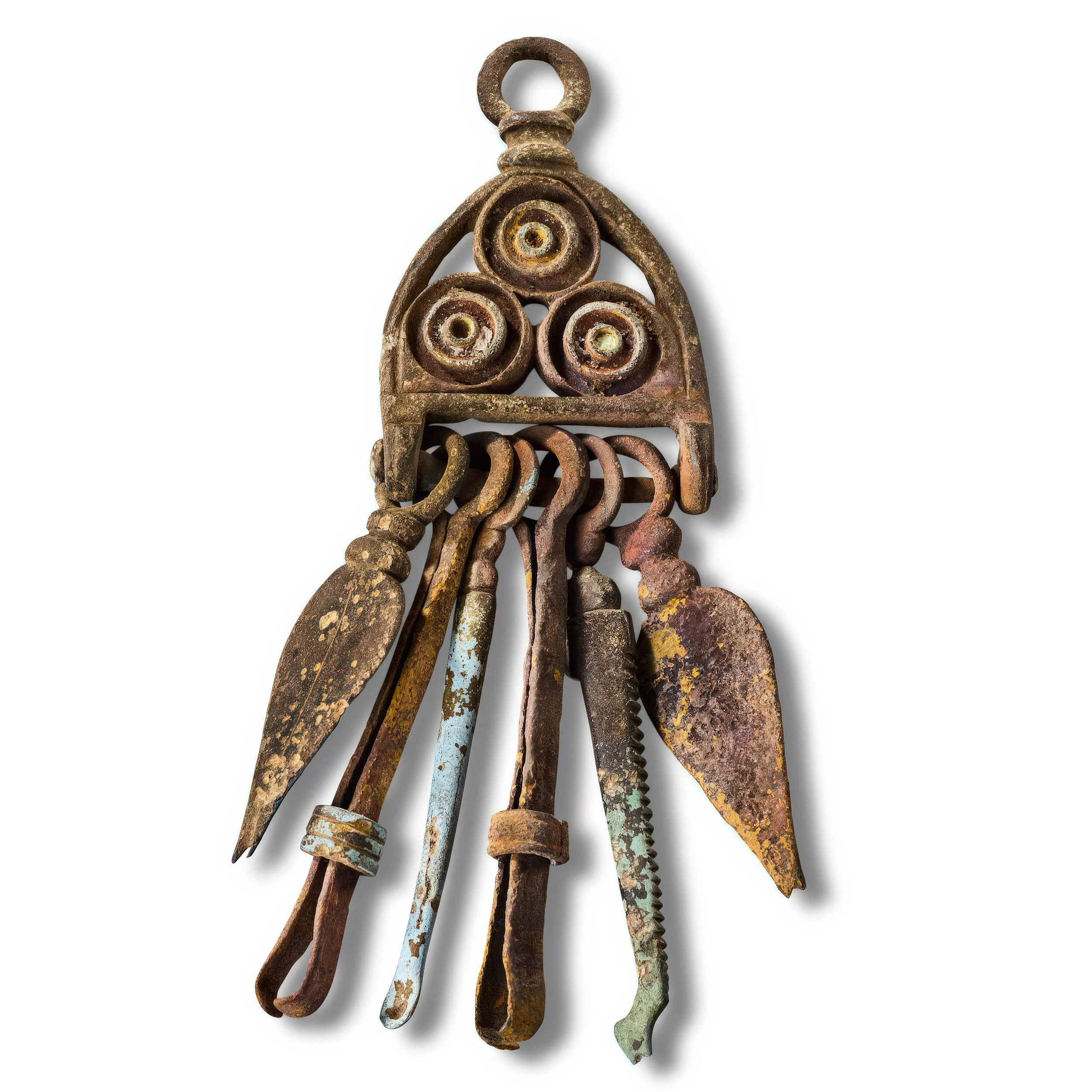 An antique set of rusty, metal kitchen or gardening tools hanging together on a white background.