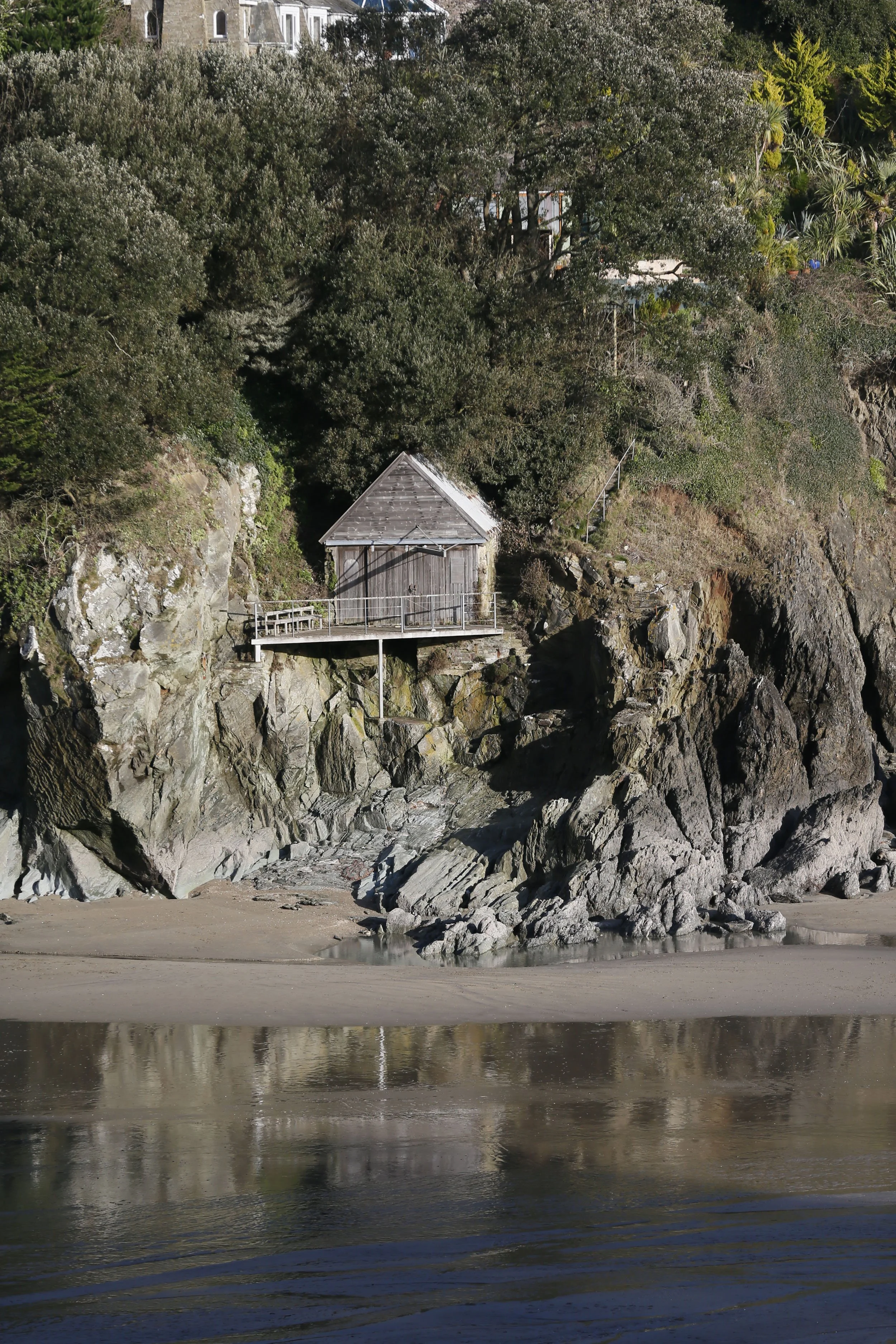 A small wooden hut built on a rocky cliffside overlooking the water, surrounded by greenery.