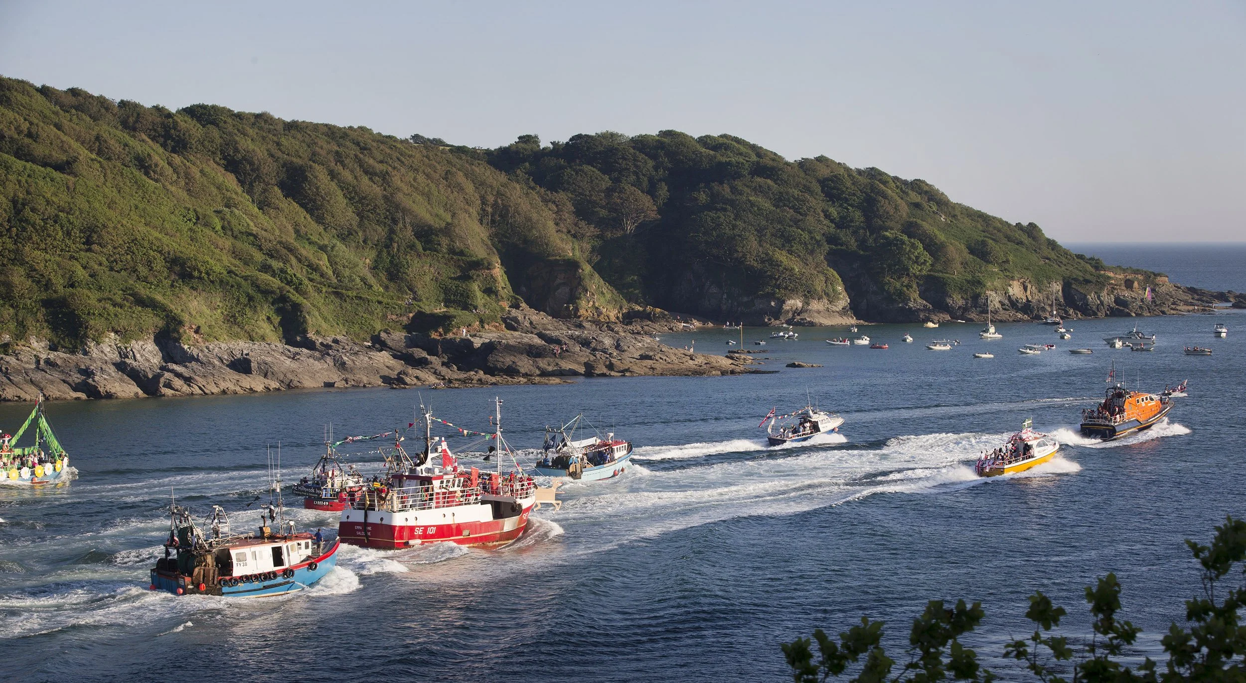 Boats sailing in a bay with a forested hillside in the background during daytime. Salcombe crabbers race during the town regatta.